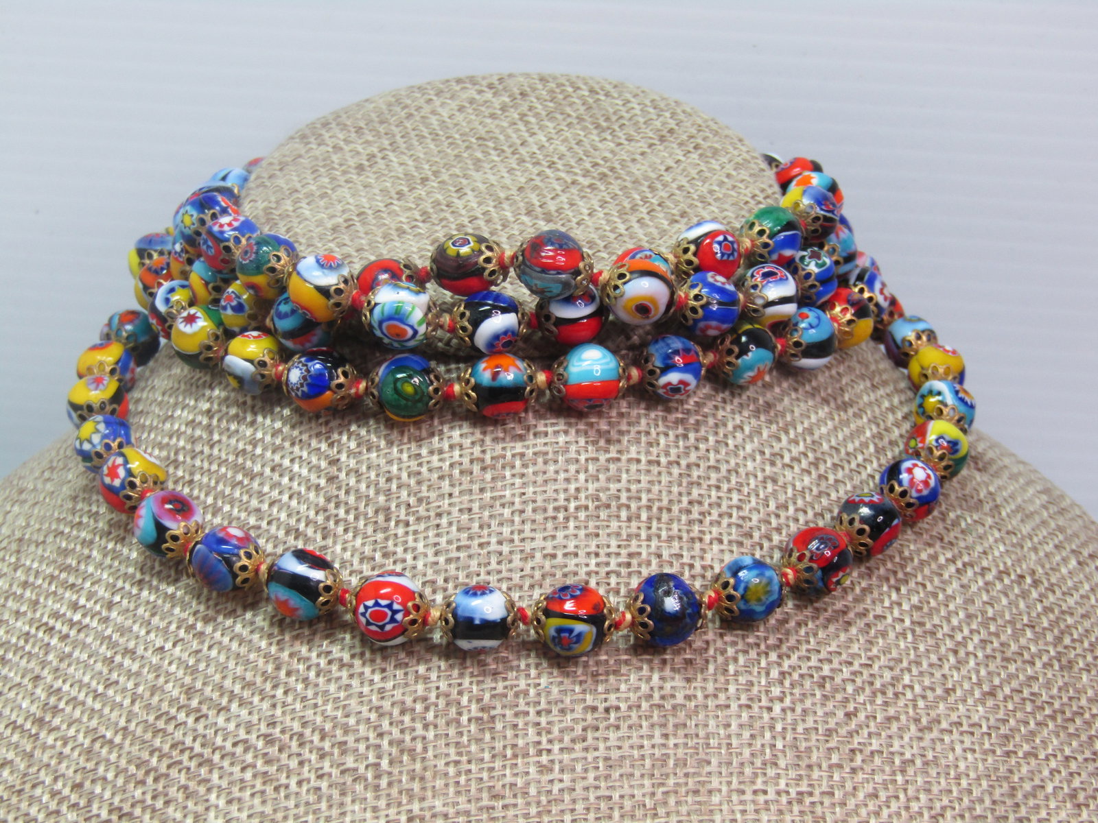 Vintage 49" Millefiori 8mm Beaded Necklace, Knotted Between Beads, 1960's.: Vintage 49" Millefiori 8mm Beaded Necklace, Knotted Between Beads, 1960's. Filigree Capped. The beads have a gold tone scalloped filigree cap on each end and are on red/white cord that is knotted betw