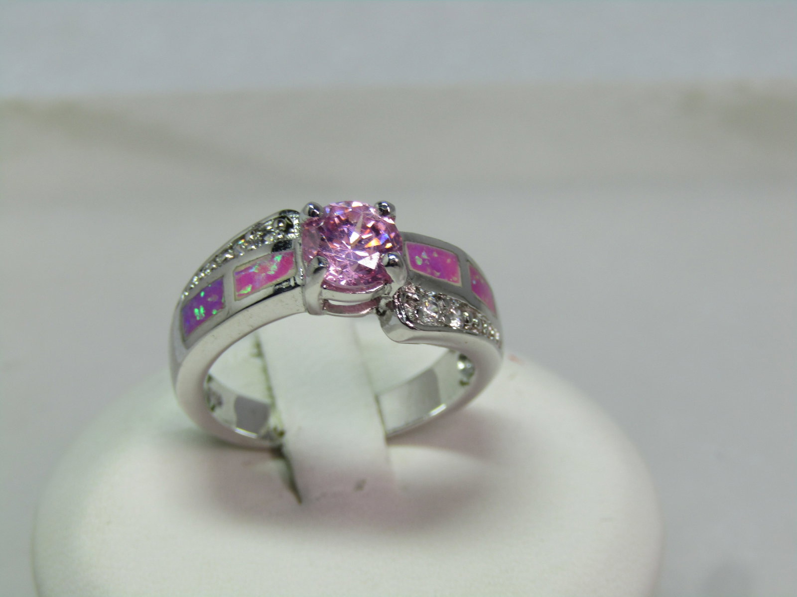 Silver Plated Faux Opal Pink Topaz Ring, Clear Rhinestones, Sz. 6.75, 1990's: Silver Plated Faux Opal Pink Topaz Ring, Clear Rhinestones, Sz. 6.75, 1990's. This has a center 5.5mm pink clear glass/crystal round stone and than a somewhat bypass design with an outer tapered edge 