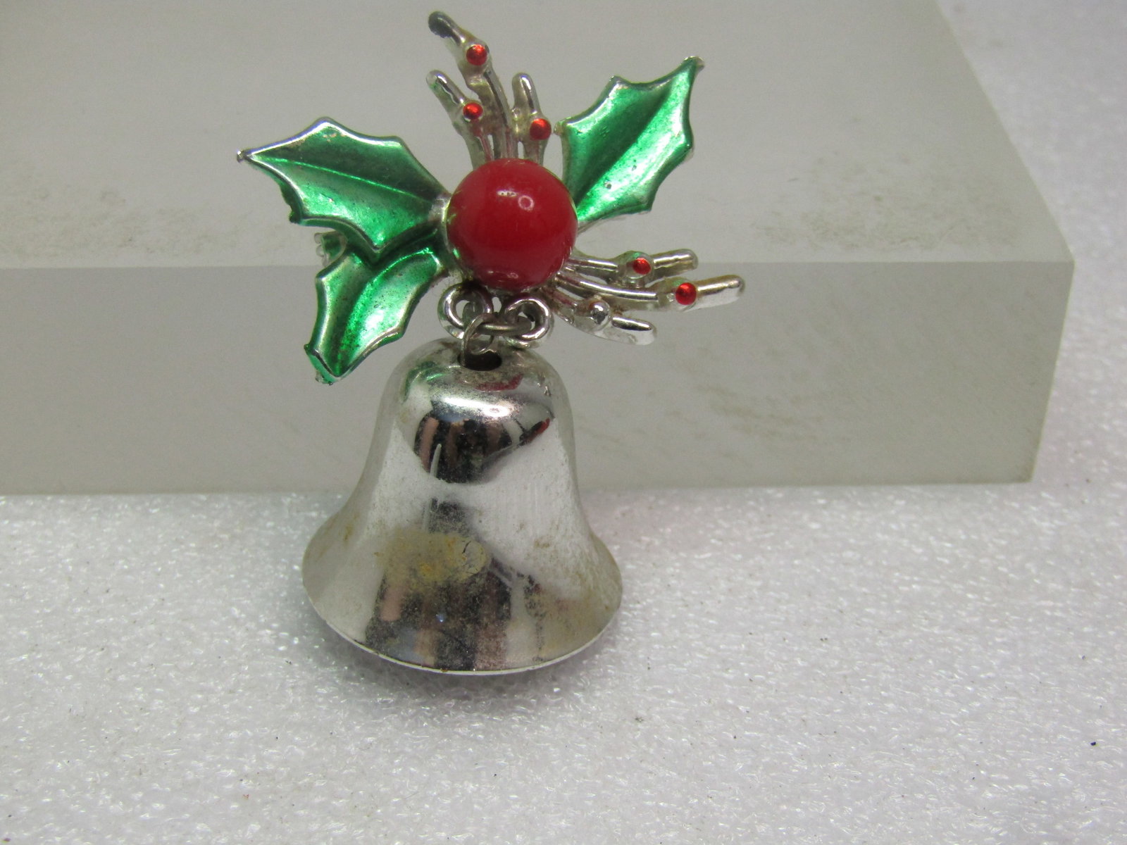 Vintage Enameled Christmas Bell Brooch with Holly, 1950's-1960's: Vintage Enameled Christmas Bell Brooch with Holly, 1950's-1960's. Silver tone with a bell that dangles from the enameled holly with a large red acrylic berry. The bell has a clapper. The brooch is app