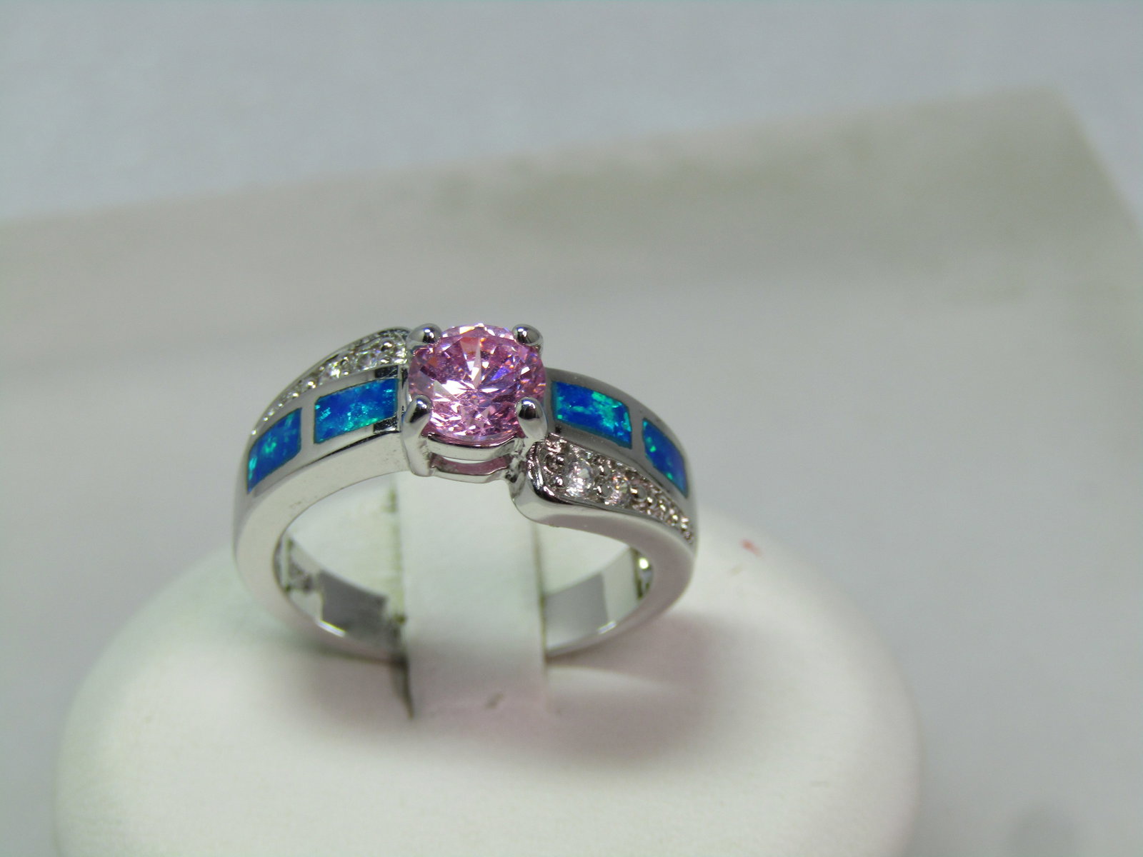 Silver Plated Faux Opal Pink Topaz Ring, Clear Rhinestones, Sz. 7, 1990's: Silver Plated Faux Opal Pink Topaz Ring, Clear Rhinestones, Sz. 7, 1990's. This has a center 5.5mm pink clear glass/crystal round stone and than a somewhat bypass design with an outer tapered edge wit