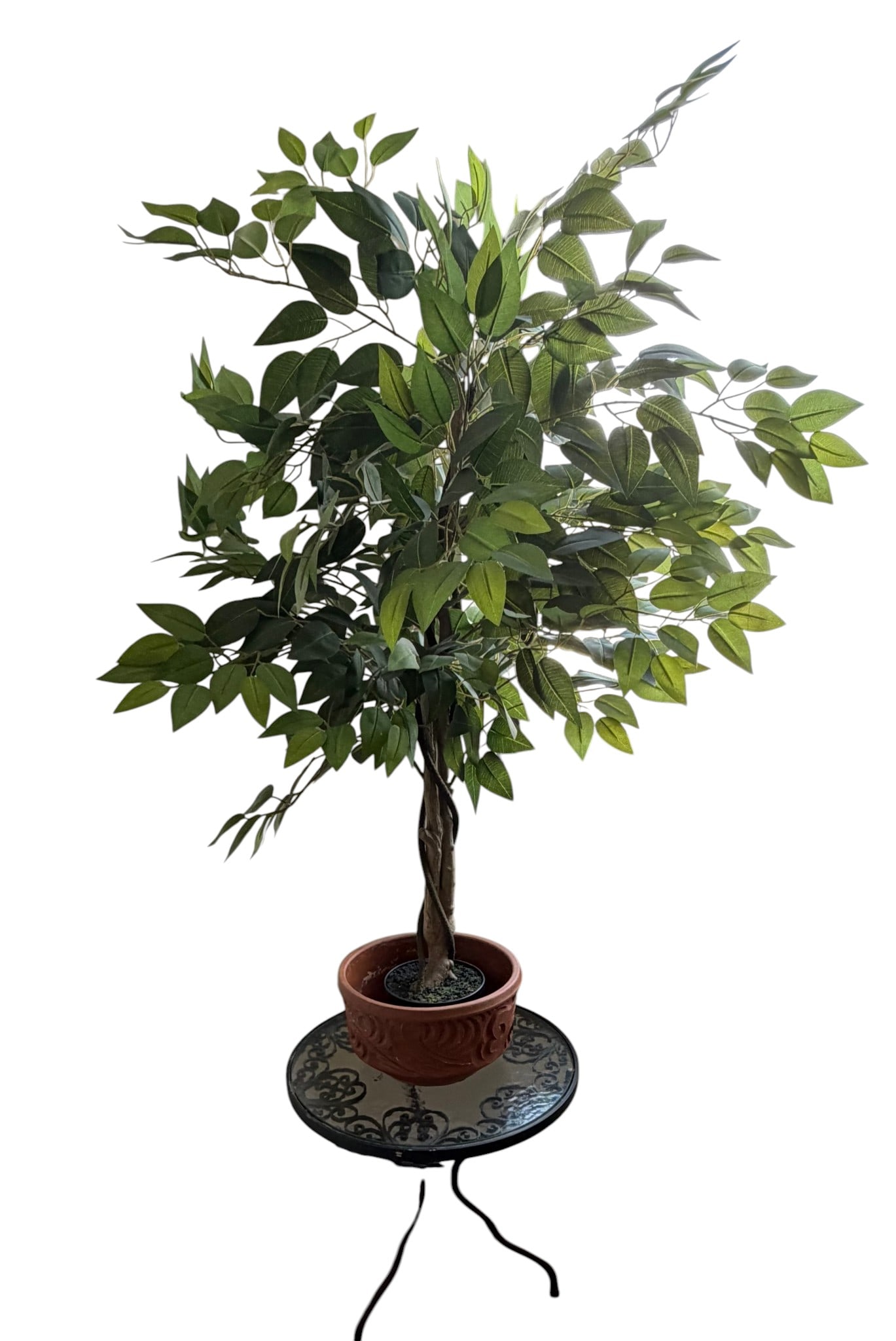 Artificial Ficus Tree in Decorative Pot on Wrought Iron Table: An artificial ficus tree, featuring realistic-looking green leaves and a twisted faux-wood trunk, housed in a decorative terracotta-colored plastic pot with an embossed scrollwork design. The plant an