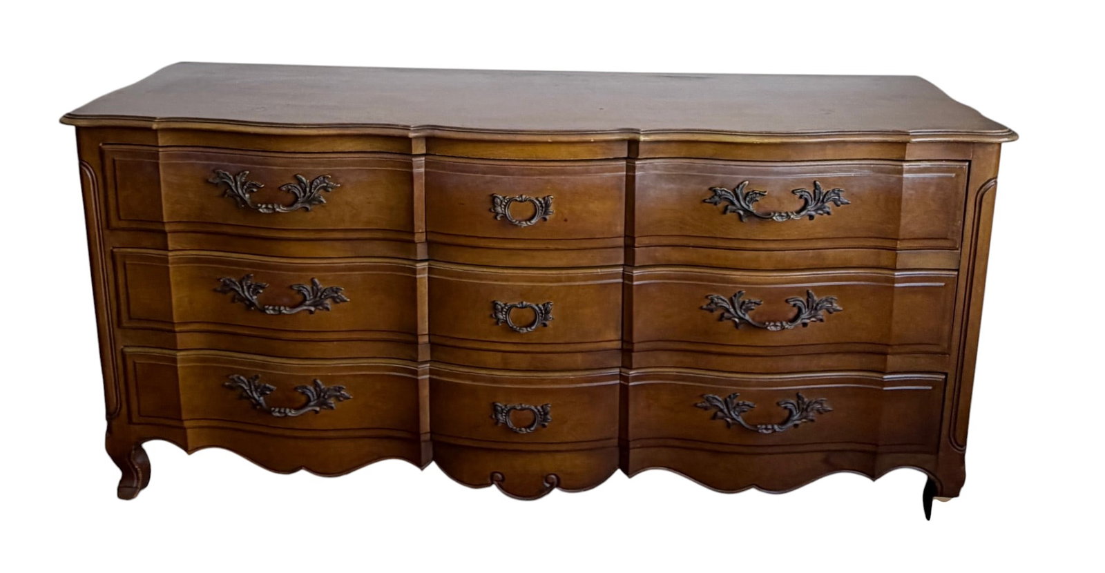 French Provincial Style Fancher Triple Dresser: A charming French Provincial style triple dresser by Fancher, featuring a warm pecan finish over what appears to be solid wood and veneers. The dresser showcases a serpentine front with nine dovetail