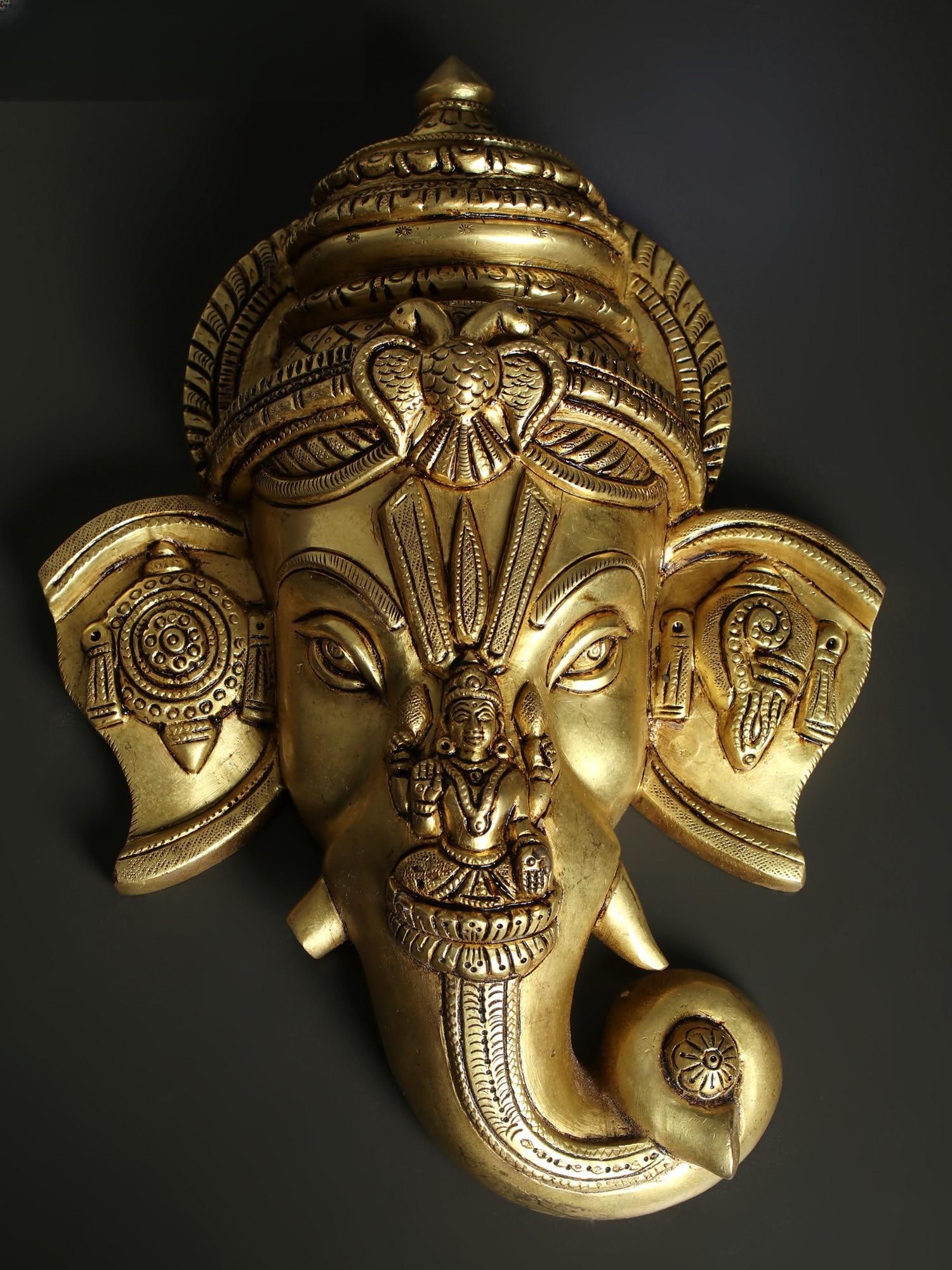 12" Brass Lord Ganesha Wall Hanging Mask with Goddess Lakshmi: Title: 12" Brass Lord Ganesha Wall Hanging Mask with Goddess Lakshmi Description: There have been rare instances when a sacred object has been further sanctified by adding more divine images. This Bra