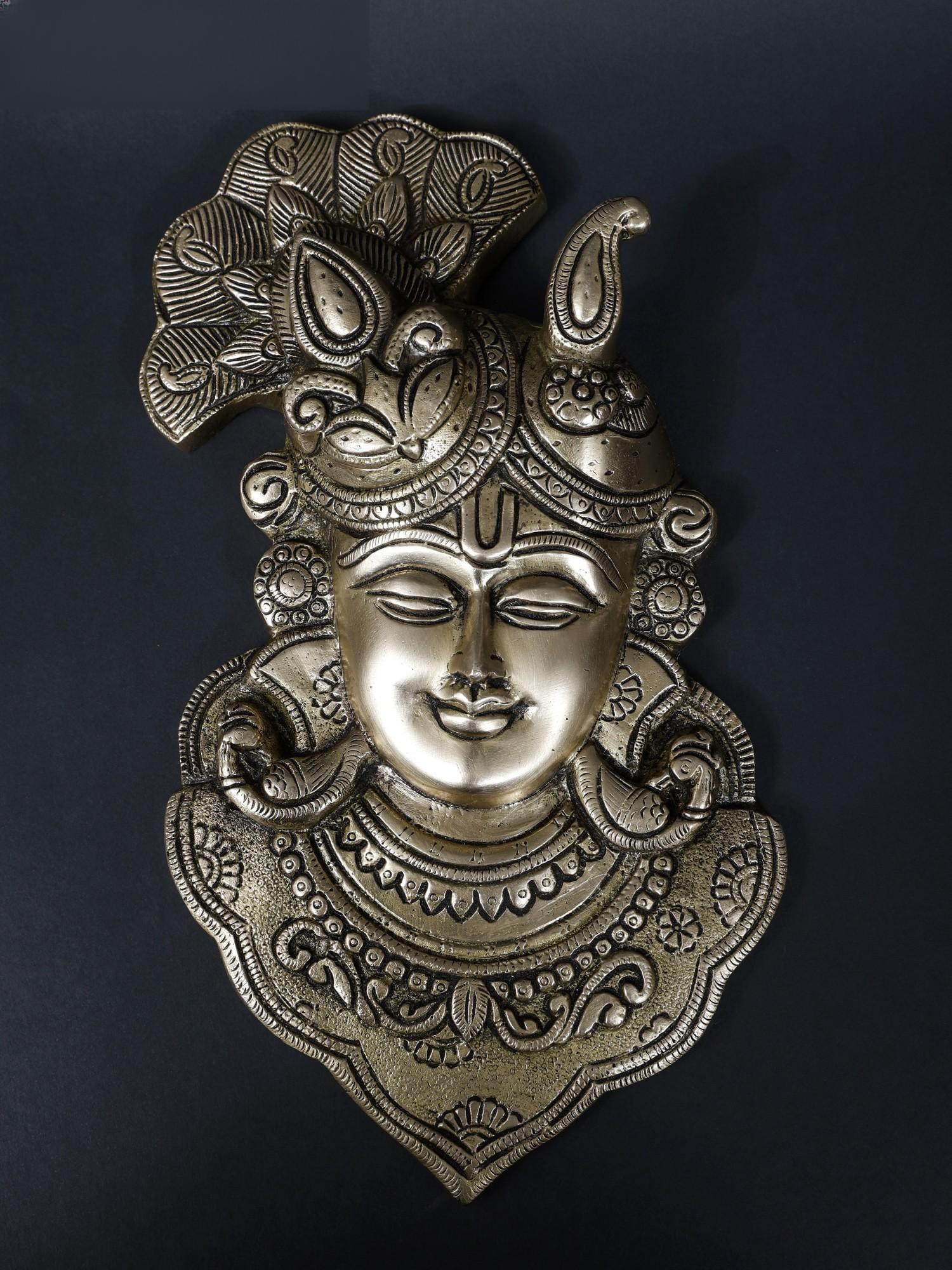 11" Brass Lord Krishna Wall Hanging Statue: Title: 11" Brass Lord Krishna Wall Hanging Statue Description: This Brass Lord Krishna Wall Hanging Statue is a serene depiction capturing Lord Krishna with closed eyes, seemingly immersed in the
