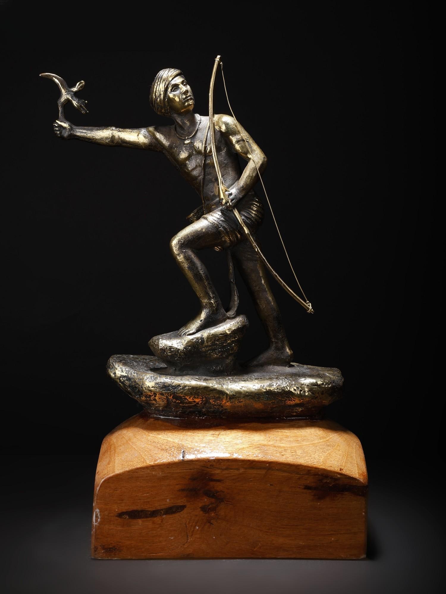 14" Handcrafted Birsa Munda Statue: Title: 14" Handcrafted Birsa Munda Statue Description: This Brass, Wood, and Stone sculpture portrays Birsa Munda in a powerful stance, standing on stone, leading with resolve and determination. With