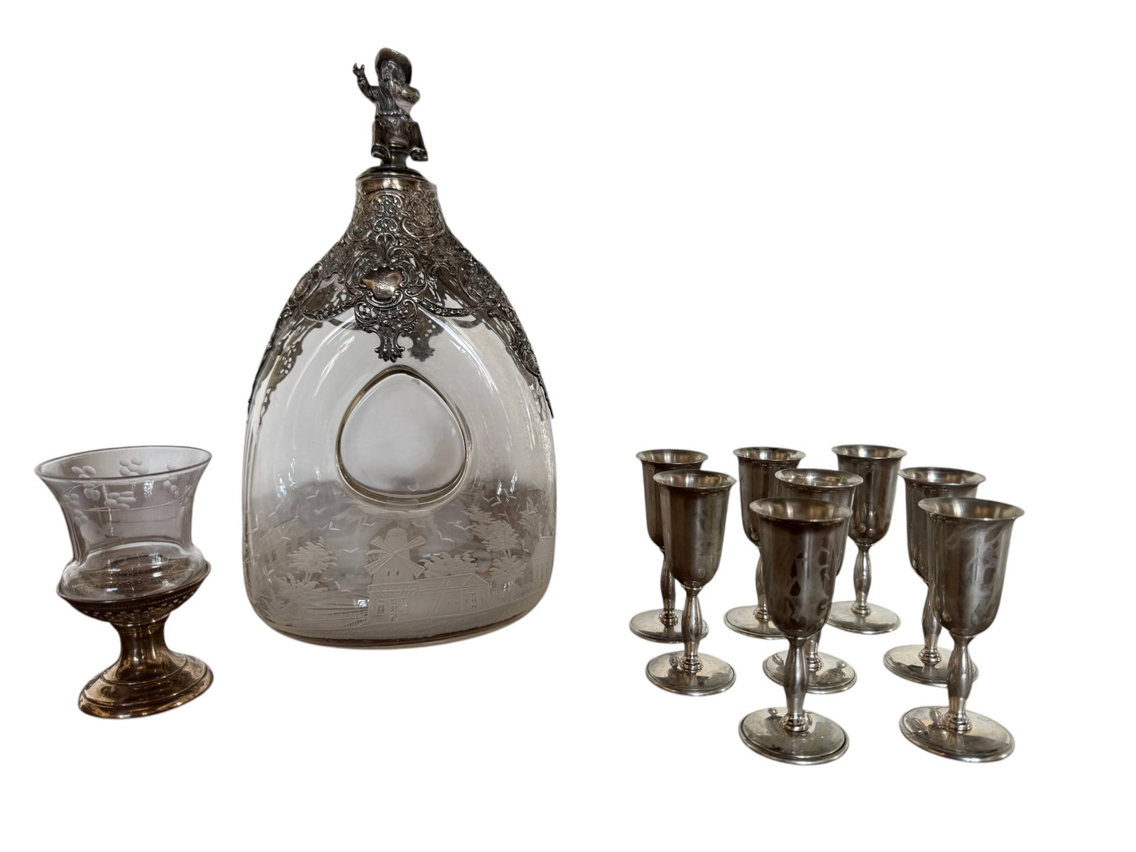 Sterling Silver Mounted Decanter by M.B. & Co. with Six Sterling Silver Miniature Goblets: A remarkable sterling silver mounted glass decanter by M.B. & Co. (likely M.B. & Co. Ltd., Manchester) featuring an intricately engraved silver overlay with a figural stopper depicting a gentleman in