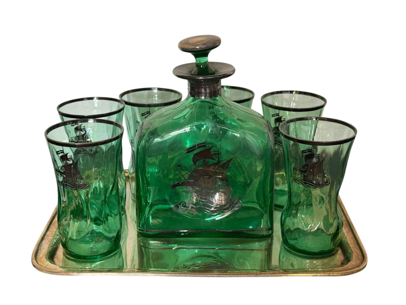 Green Glass Decanter Set with Silver Overlay and Nautical Motif on Silverplate Tray: A charming six-piece green glass decanter set, featuring a decanter with stopper and five matching glasses, all adorned with a silver overlay depicting a nautical ship motif. The set is presented on