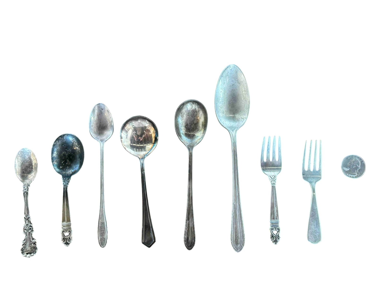 Collection of Assorted Sterling Silver Flatware (9 Pieces): A collection of nine pieces of sterling silver flatware, featuring a variety of patterns and styles. The lot includes five spoons of varying sizes and designs, and two forks that appear to be from the
