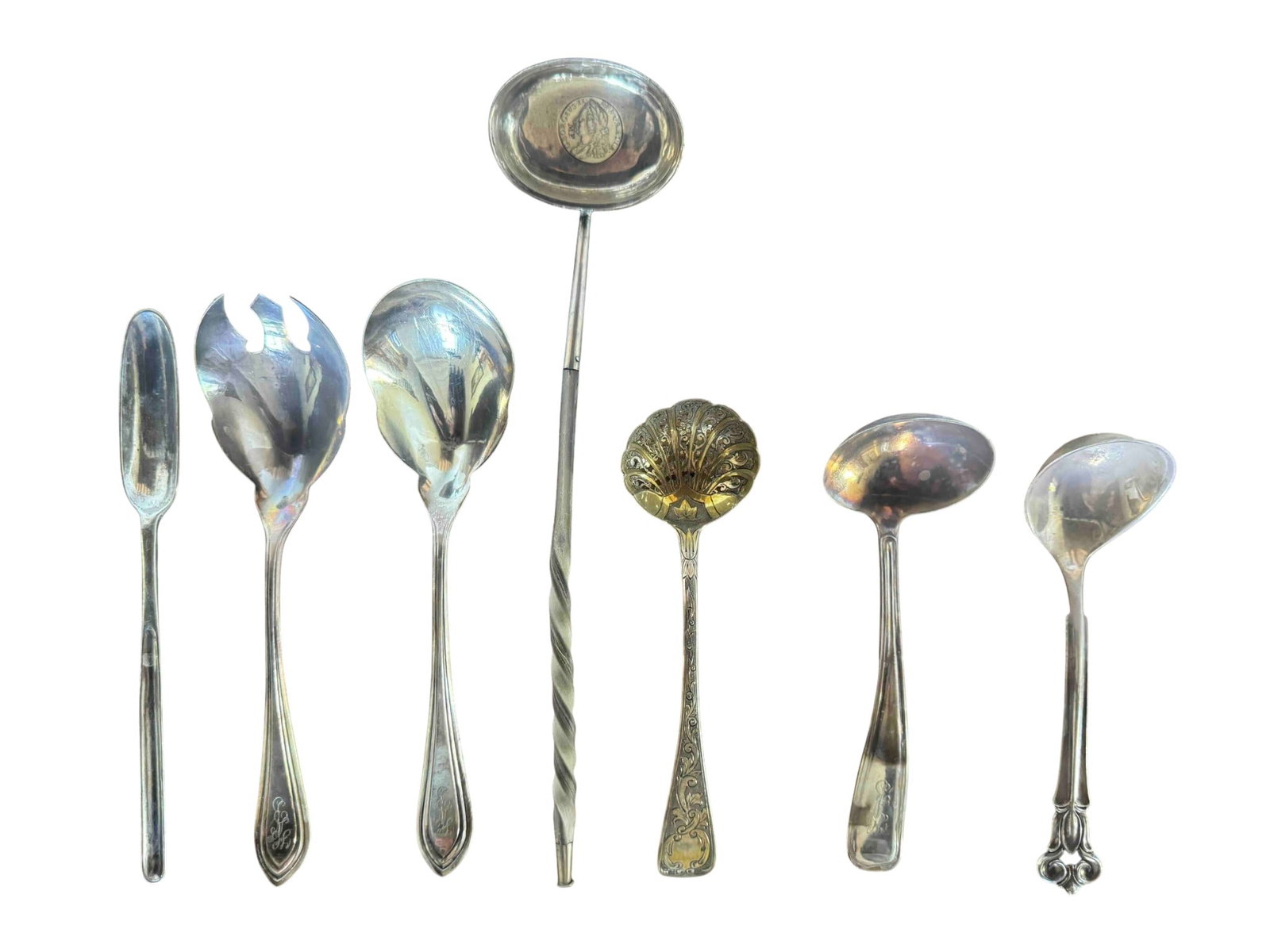 Collection of Assorted Sterling Silver Serving Utensils: An eclectic collection of seven sterling silver serving utensils, likely dating from the late 19th to early 20th century, showcasing various styles and designs. The set includes a large ladle with a