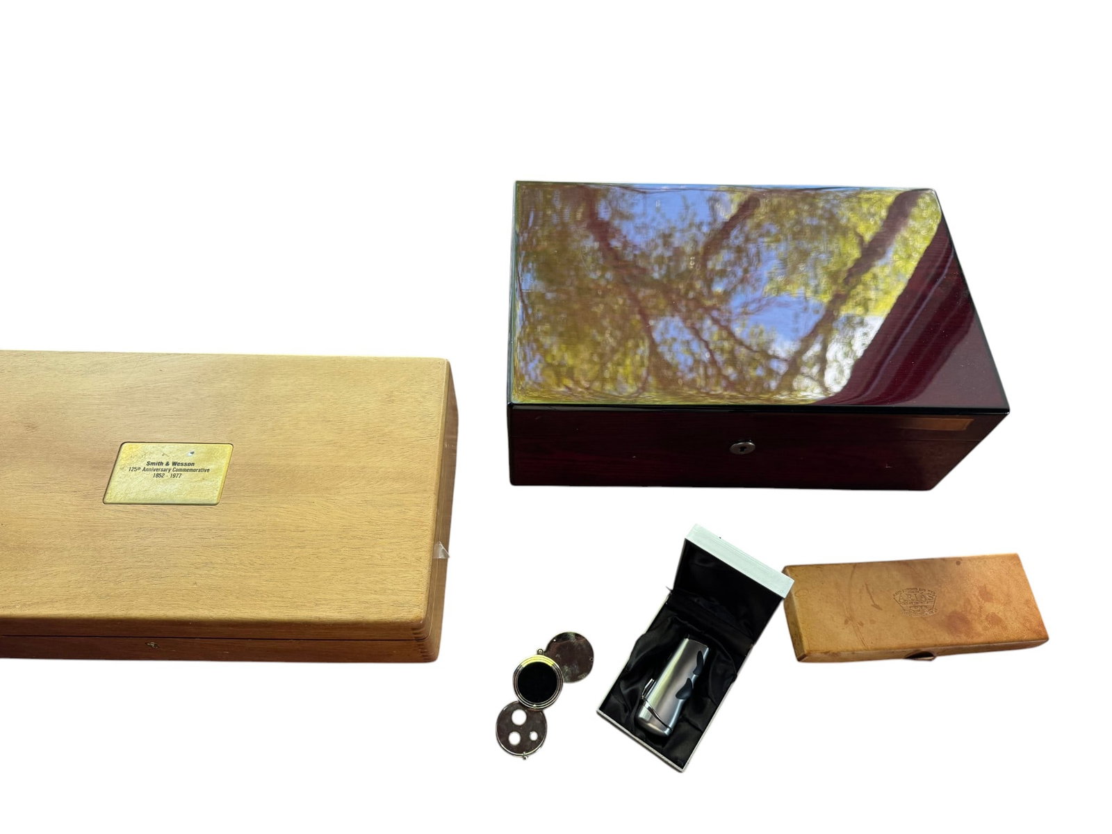 Collection of Humidors, Lighter, and Pill Box: A collection of a highly polished dark wood humidor, a light wood humidor with a "Smith & Wesson .357 Magnum Ammunition" brass plaque, and a light wood box with an indistinct lid stamp. Also includes