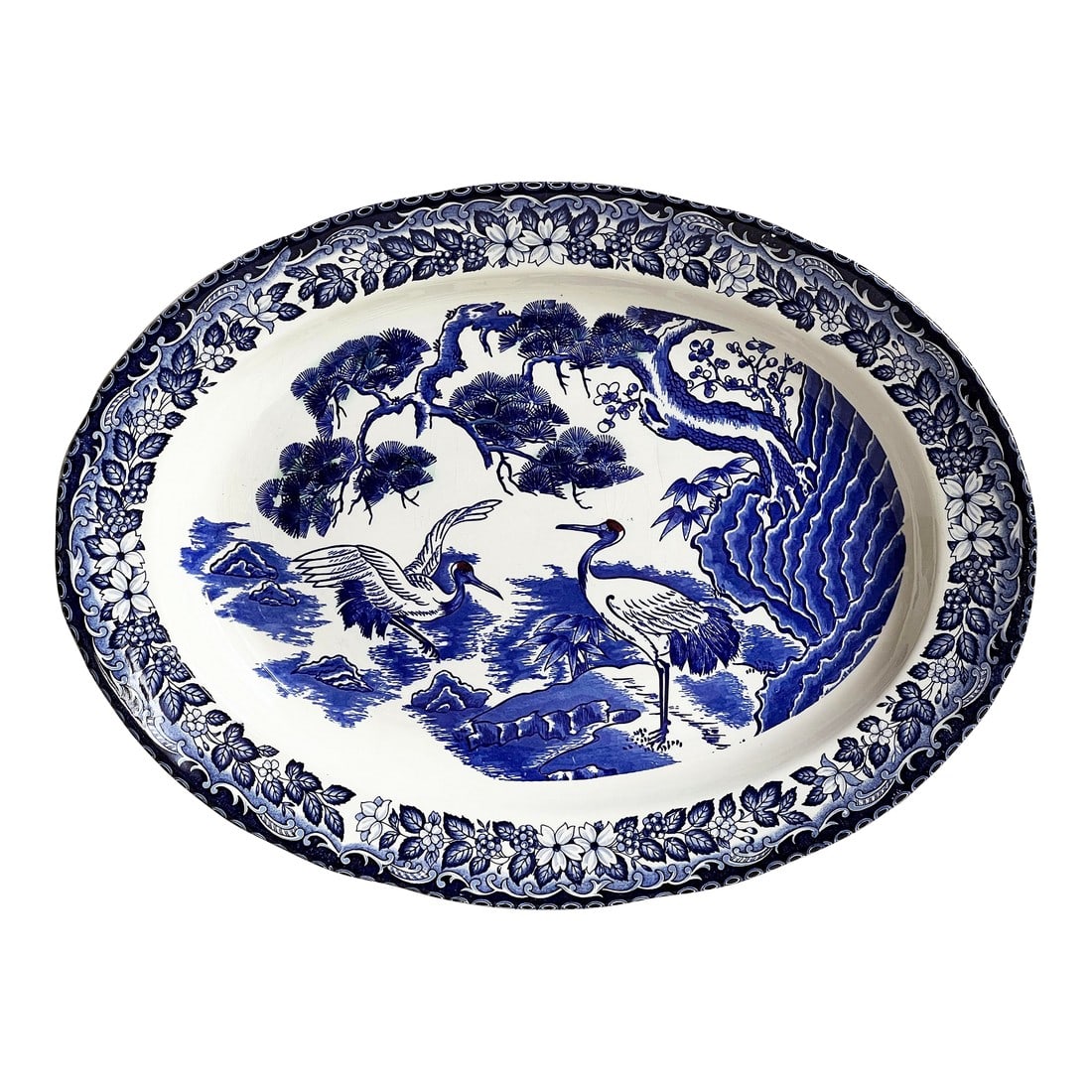 Antique Japanese Blue and White Porcelain Serving Platter With Cranes and Tree: This large late 19th or early 20th century Japanese porcelain platter features a richly detailed blue and white landscape with cranes among pine trees and stylized waves, framed by a dense floral bord