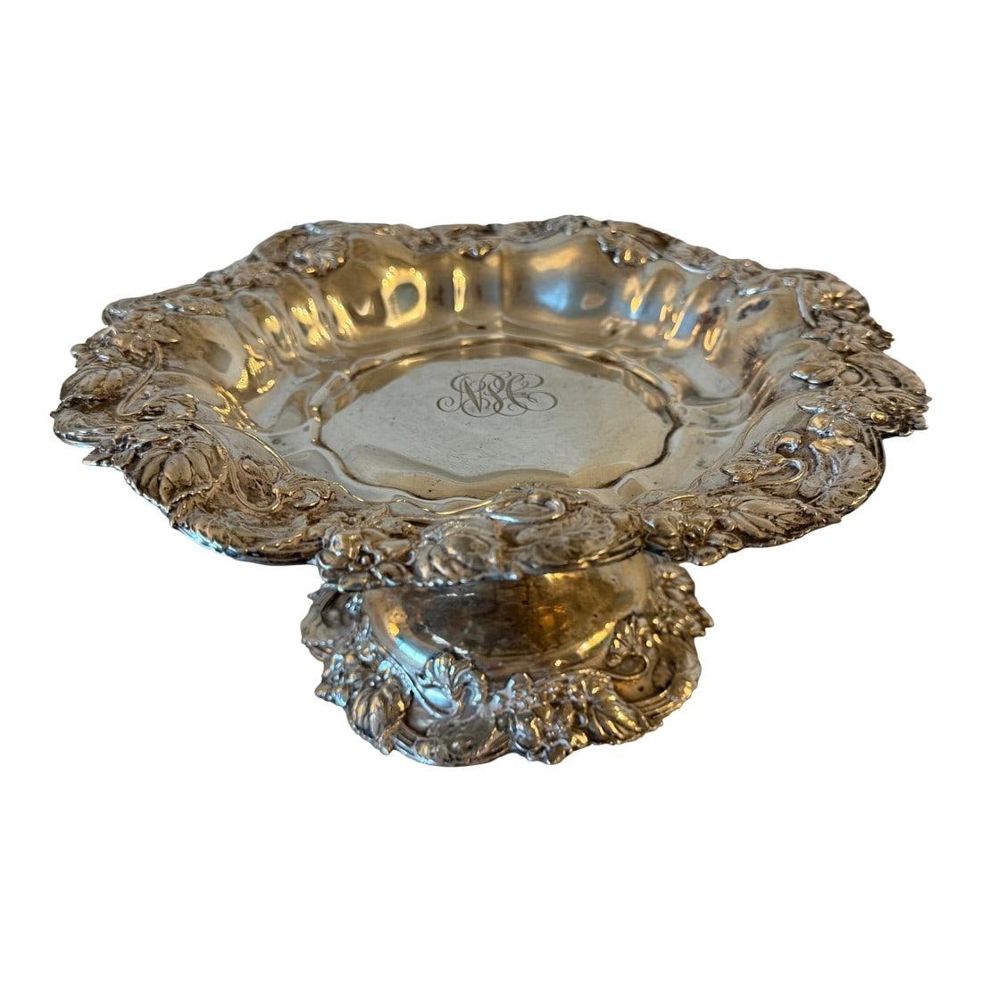 Antique Footed Sterling Silver Plate With Floral Design 570g: Antique footed sterling silver plate marked 7000, decorated with elegant floral designs along the rim and foot. The raised form and detailed floral ridges give this piece a classic, refined look.