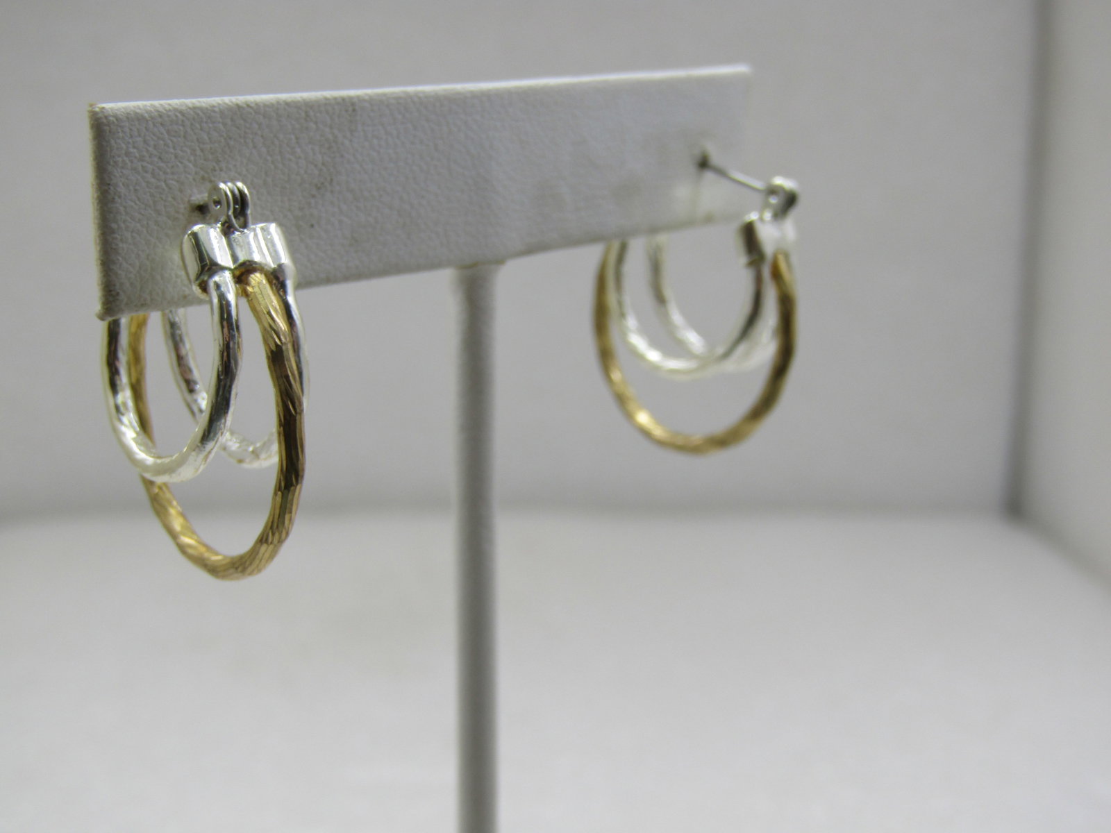 Two Tone Staggered Hoop Earrings, Pierced, 1": Two Tone Staggered Hoop Earrings, Pierced, 1". The hoops have a textured finish and are gold tone and silver tone. The larger hoop is gold tone and 1" long, there is a shorter silver tone hoop on each