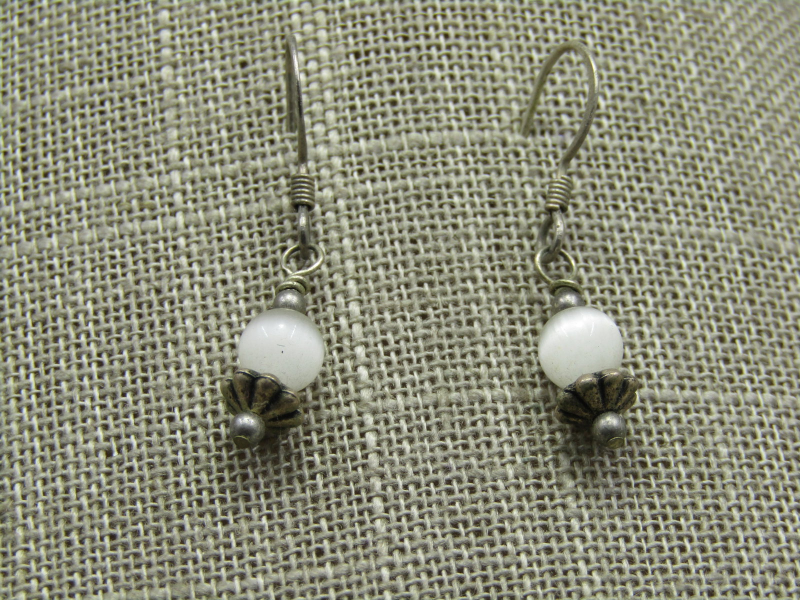 Vintage White Cat Eye Boho Earrings, Pierced: Vintage White Cat Eye Boho Earrings, Pierced, appx. 1.25" long from curve in hook post. Fluted and silver tone accent beads. The white cateye round bead is appx. 5mm. They do not test as sterling. Ver