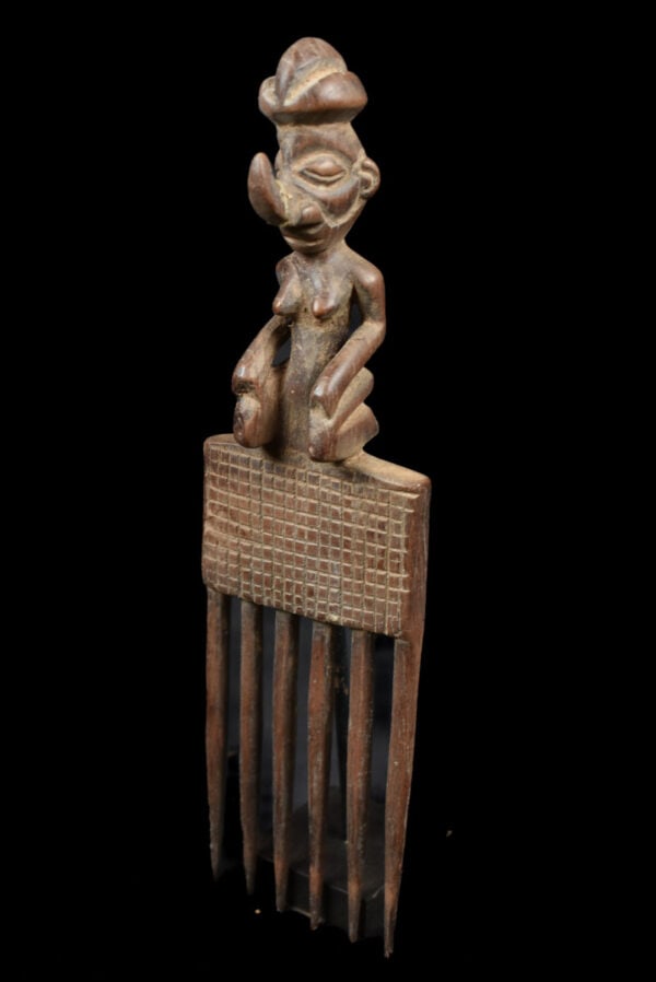 Comb – Wood – Yaka – DR Congo: Detailed wooden comb with great patina from the Yaka tribe of DR Congo. Typical ancestor figure is sitting on top of the comb with an upturned recognisable Yaka nose. Good condition with traces of