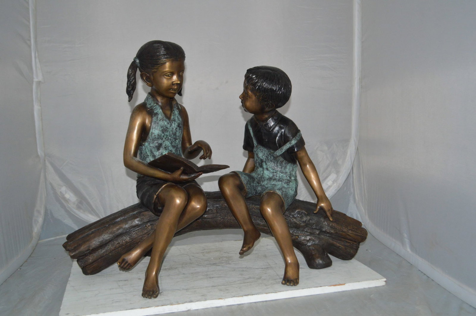 Boy and Girl on a tree log reading Bronze Statue - Size: 37"L x 14"W x 27"H. - 4