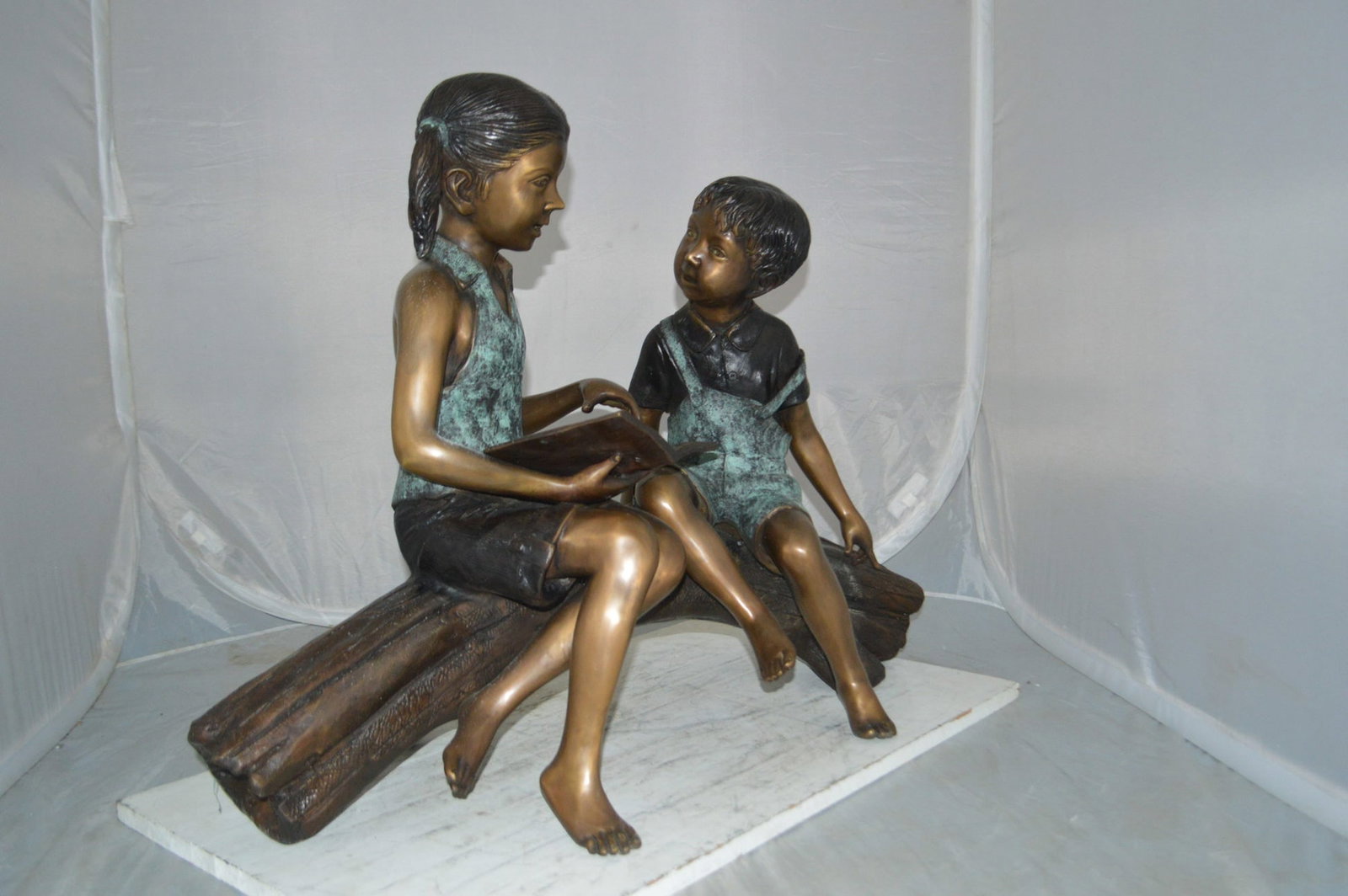 Boy and Girl on a tree log reading Bronze Statue - Size: 37"L x 14"W x 27"H. - 6