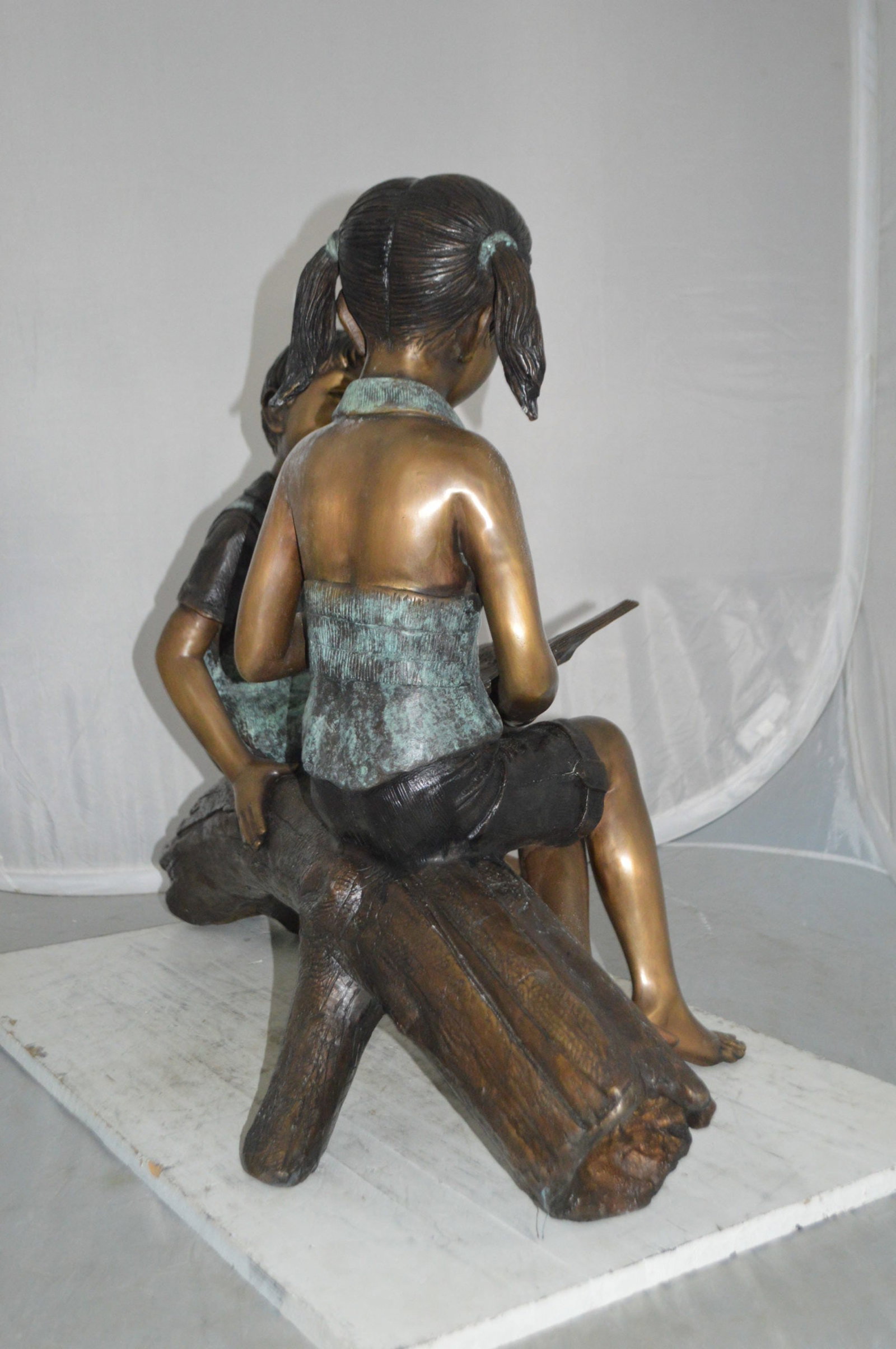 Boy and Girl on a tree log reading Bronze Statue - Size: 37"L x 14"W x 27"H. - 8