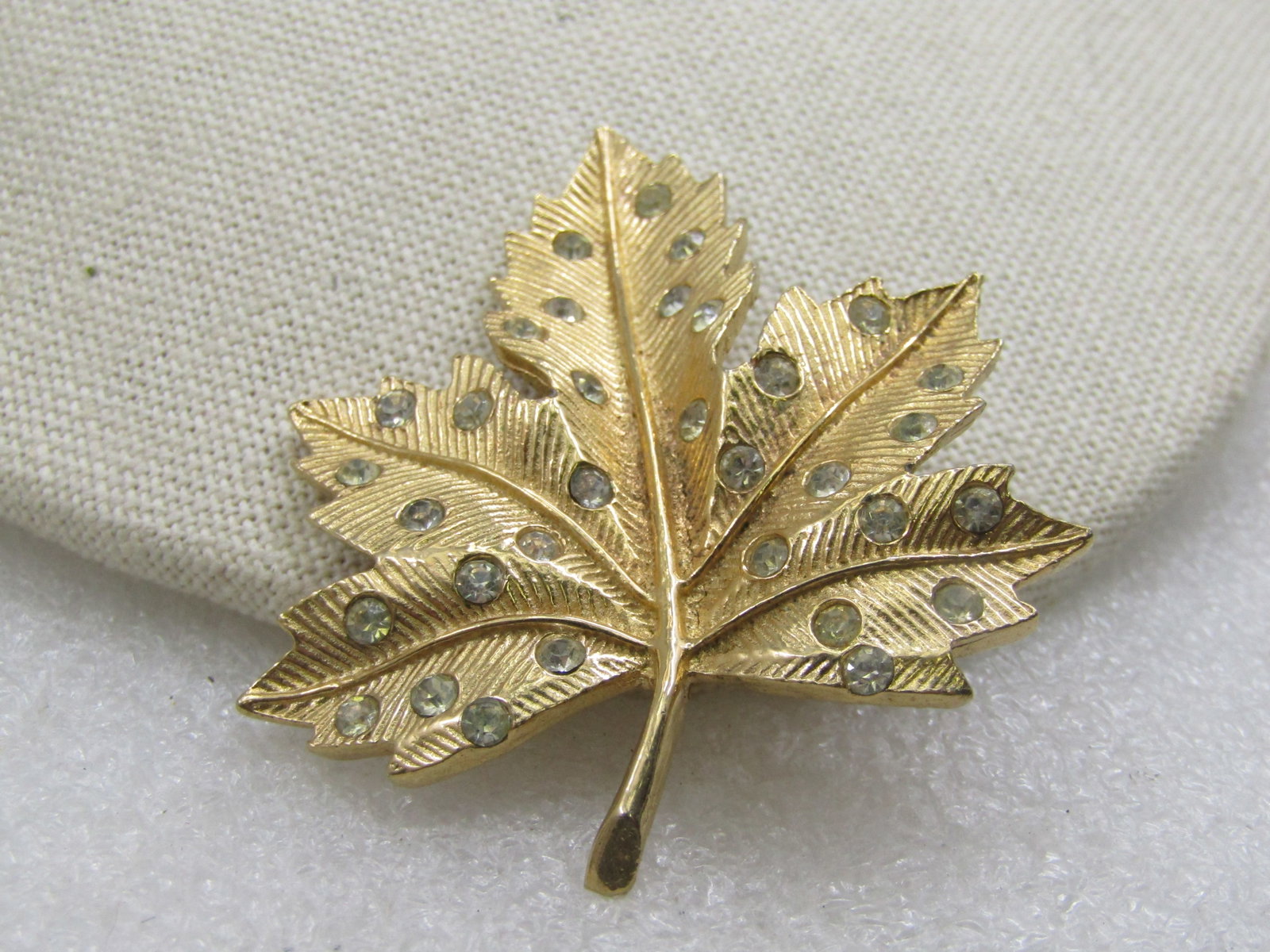 Vintage Gold Tone Rhinestone Leaf Brooch, 1960's: Vintage Gold Tone Rhinestone Leaf Brooch, 1960's. Ridged textured design with smooth veining that is raised down the center of the leave and the sections of the leave. The rhinestones are set into the