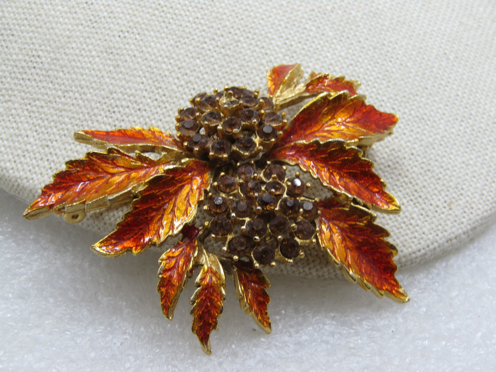 Vintage Burnt Orange Enameled Rhinestone Leaf Brooch, 1960's-1970s: Vintage Burnt Orange Enameled Rhinestone Leaf Brooch, 1960's-1970s. Gold tone metal with orange and burnt orange enameling and two blossom like accents with shades of smoky/amber rhinestones, round, a