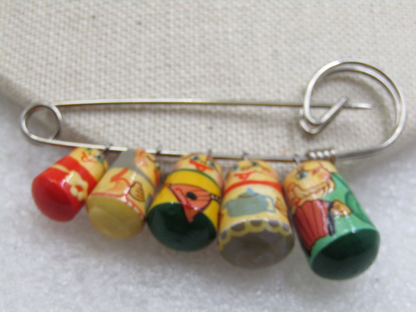 Hand Painted Graduated Family Beaded Brooch, Stacking Doll Style: Hand Painted Graduated Family Beaded Brooch, Stacking Doll Style. 2.75" style ornated safety pin topper with five famiy members, hand painted in the style of Russian dolls. each wooden bead is slightl