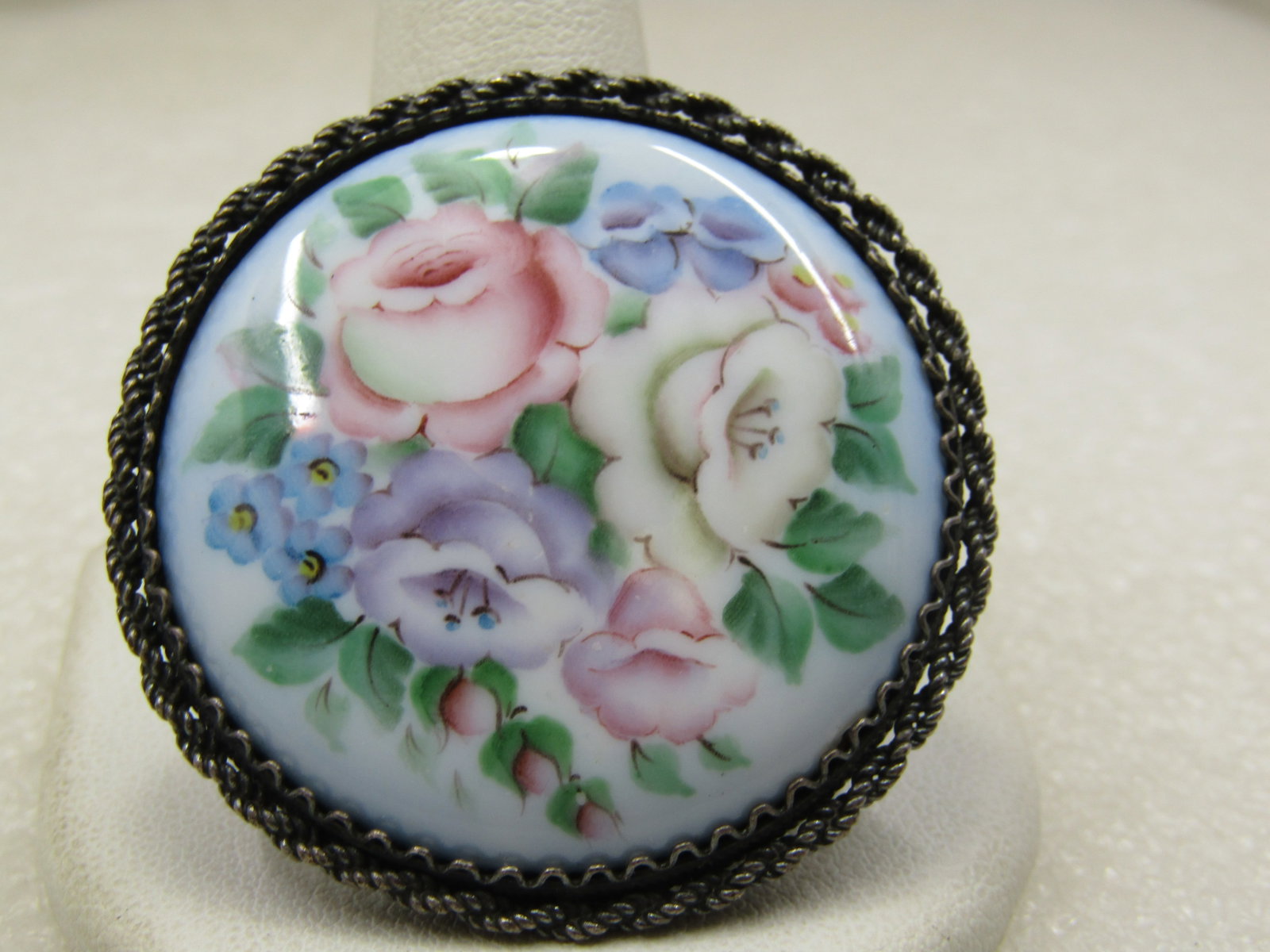 Vintage Floral Ceramic/Porcelan Round Brooch, C-Clasp1-5/8": Vintage Floral Ceramic/Porcelan Round Brooch, C-Clasp1-5/8" ewith twised rope edge and zigzag wire bezel around the center piece. The metal does not test as sterling. It is silver tone. Age is estimat
