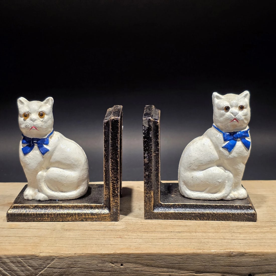 Pair of Cast Iron White Cat Bookends: Wonderful matching pair of reproduction heavy cast iron bookends featuring seated cats with slightly serious expressions. Each cat is painted white with a bright blue bow at the neck and is mounted