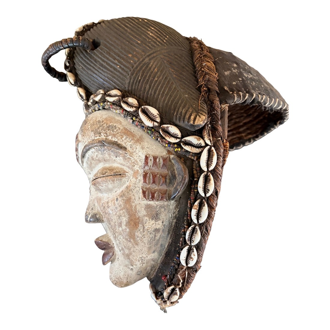 Punu Mask 20th Century: This is a 20th century Punu mask from Gabon. This vintage mask is made from wood, textiles and cowrie shells. It is white, and brown in color. It shows signs of faded patina due to aging. It measures 