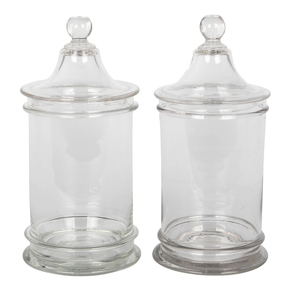 French Glass Apothecary Jars or Canister Pair: A pair of French hand-blown clear glass lidded apothecary or candy jars. Smooth canister form with knob on lid. Perfect for use as bathroom canisters or for decorative displays of seashells, marbles o