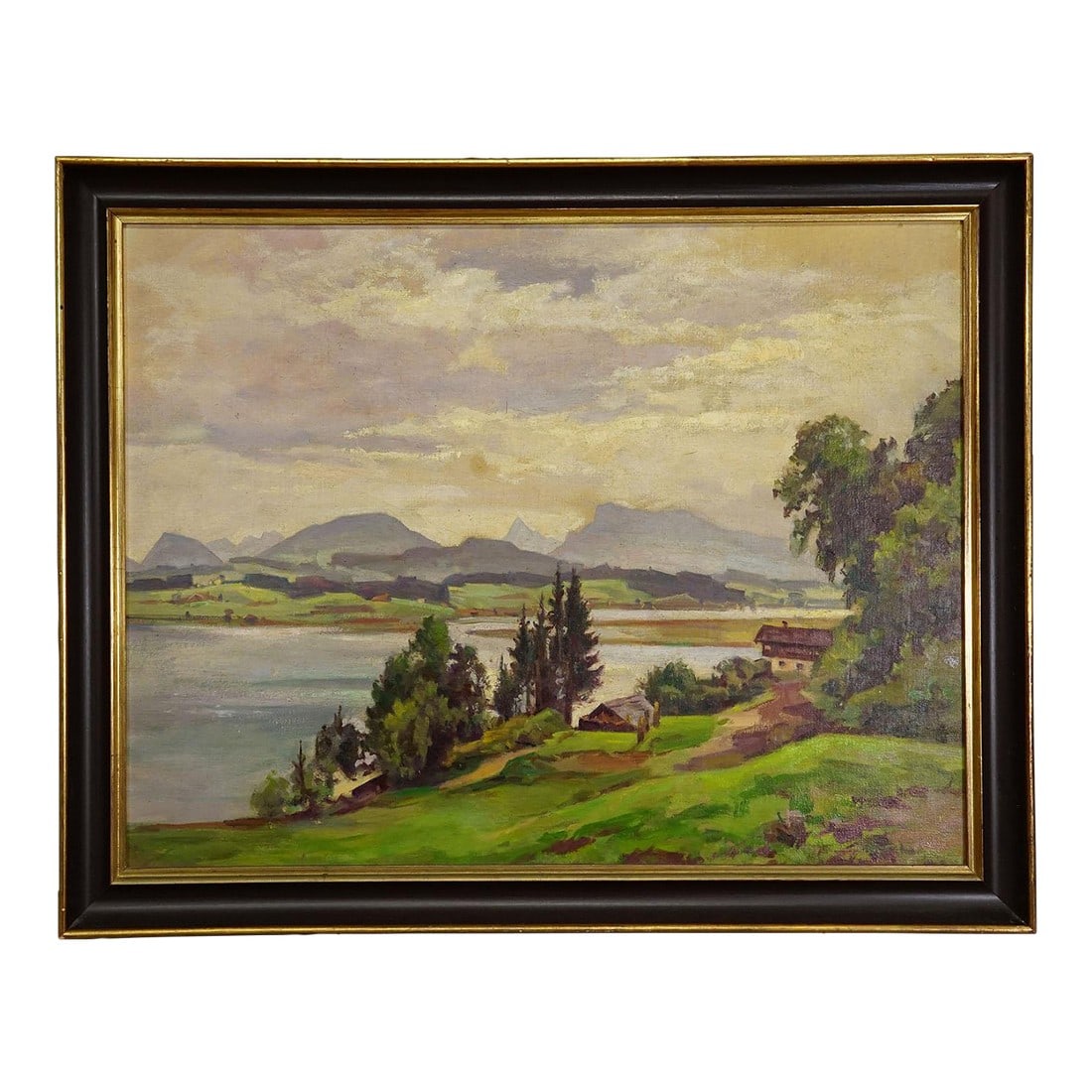Alpine Lake View Oil Painting With Tyrolean Hut: Alpine Lake View Oil Painting with Tyrolean Hut A large landscape painting in a dark brown frame with a gold inner lining. The scene features a peaceful lakeside view with gently rolling green hills, 