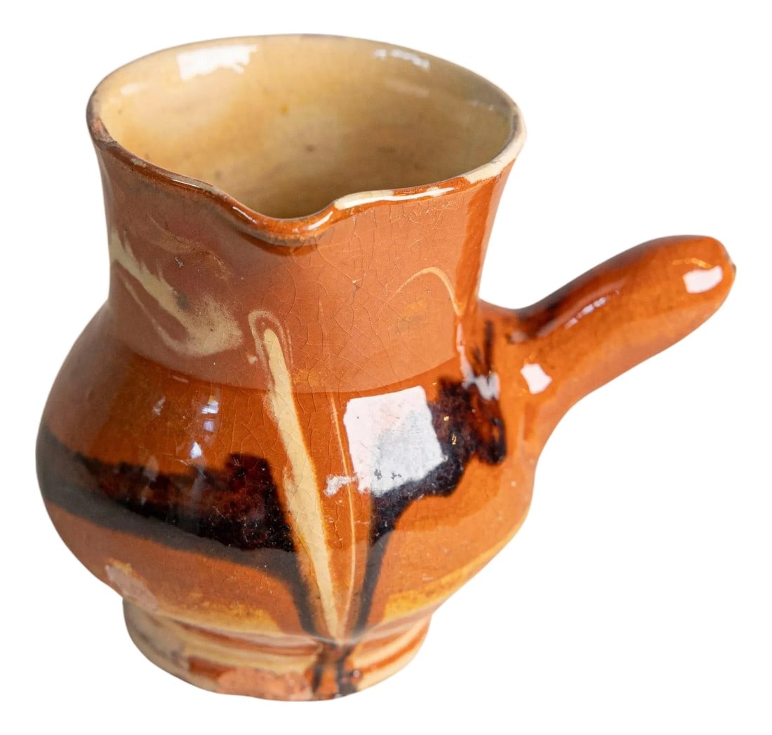 Early 20th Century French Glazed Terracotta Pitcher with Side Handle: A charming and rustic early 20th century French terracotta pitcher, hand-thrown and finished in a traditional slip-glaze technique. The piece features a small rounded body, a slightly flared rim with