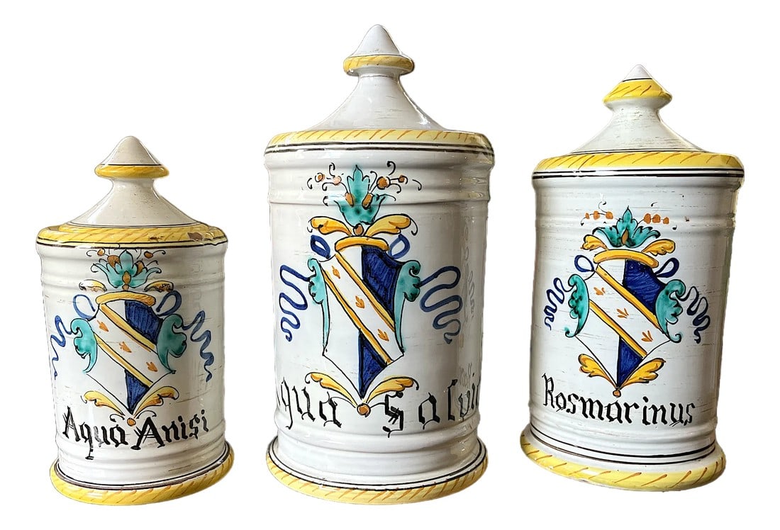 1960s Set of 3 Italian Majolica Apothecary Jars – Aqua Anisi, Rosmarinus & Aqua Salvia: A charming set of three vintage Italian majolica apothecary jars, hand-painted in classic Old World style and labeled Aqua Anisi, Rosmarinus, and Aqua Salvia. Each jar features a traditional shield-an