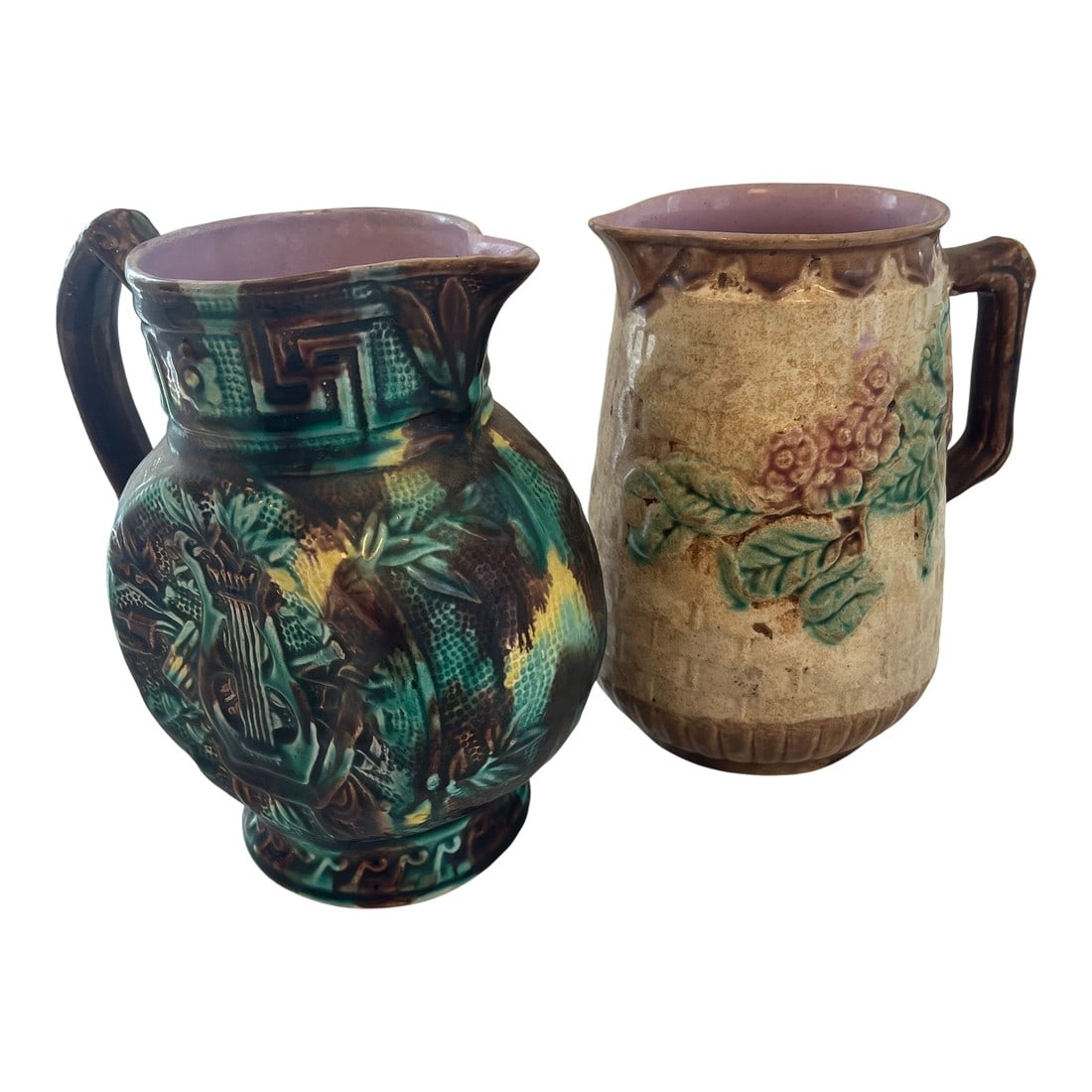 1900s Two Majolica Ceramic Pitchers: Two ceramic majolica pitchers. One in chocolate, browns greens and yellows with a harp decoration on either side the other in beige and brown with a floral and leaf decoration. Approximately the same