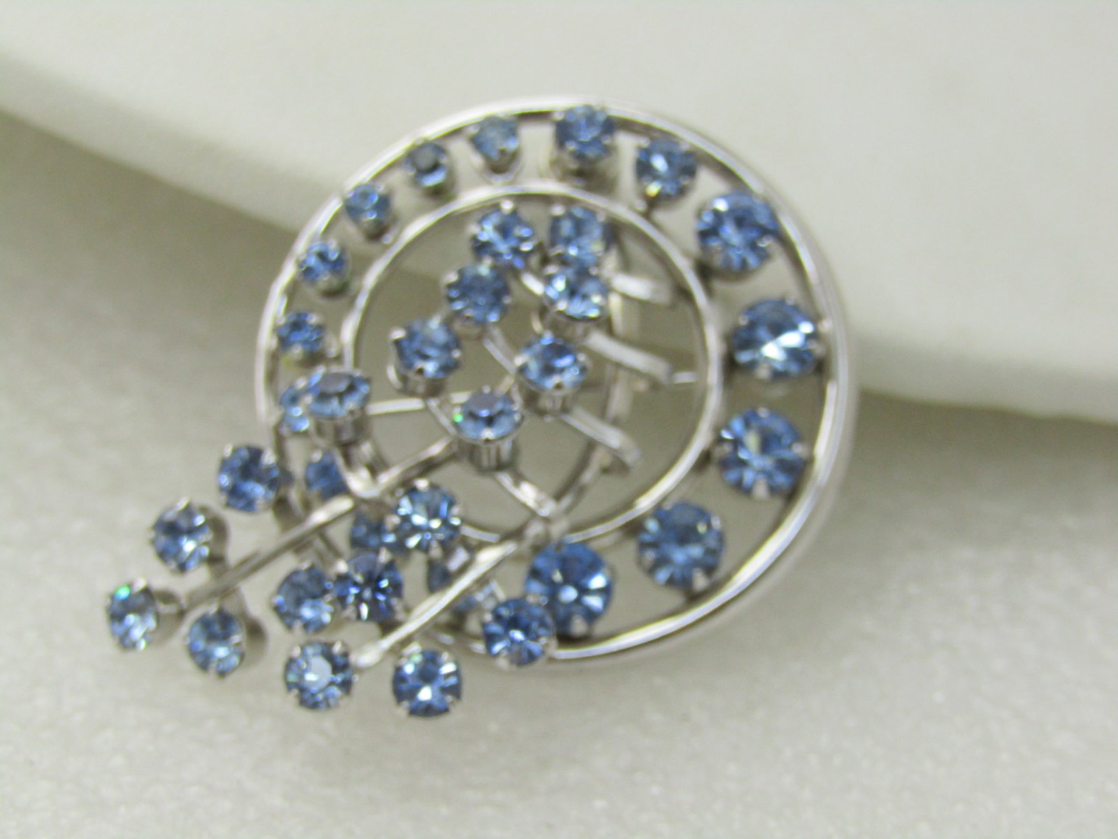 Vintage Blue Rhinestone Circle & Trail Brooch, 1960's, 1.75", Silver Tone: Vintage Blue Rhinestone Circle & Trail Brooch, 1960's, 1.75", Silver Tone. Two stem-like trails pass through the center of the circle of blue rhinestones and cross over the edge and extend beyong the 