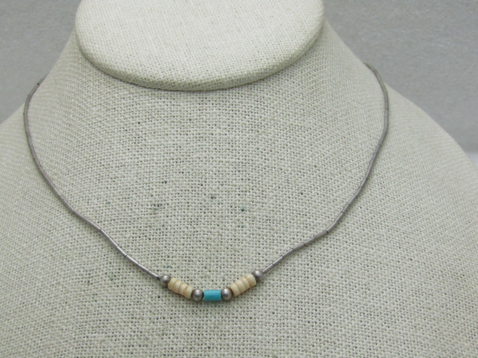 Sterling Southwestern Puka Turquoise Beaded Necklace 16": Sterling Southwestern Puka Turquoise Beaded Necklace 16". Straw liquid silver beads that are appx. 1mm wide with a centr of 8 puka shells and a single turquoise barrel bead with silver beads. The barr