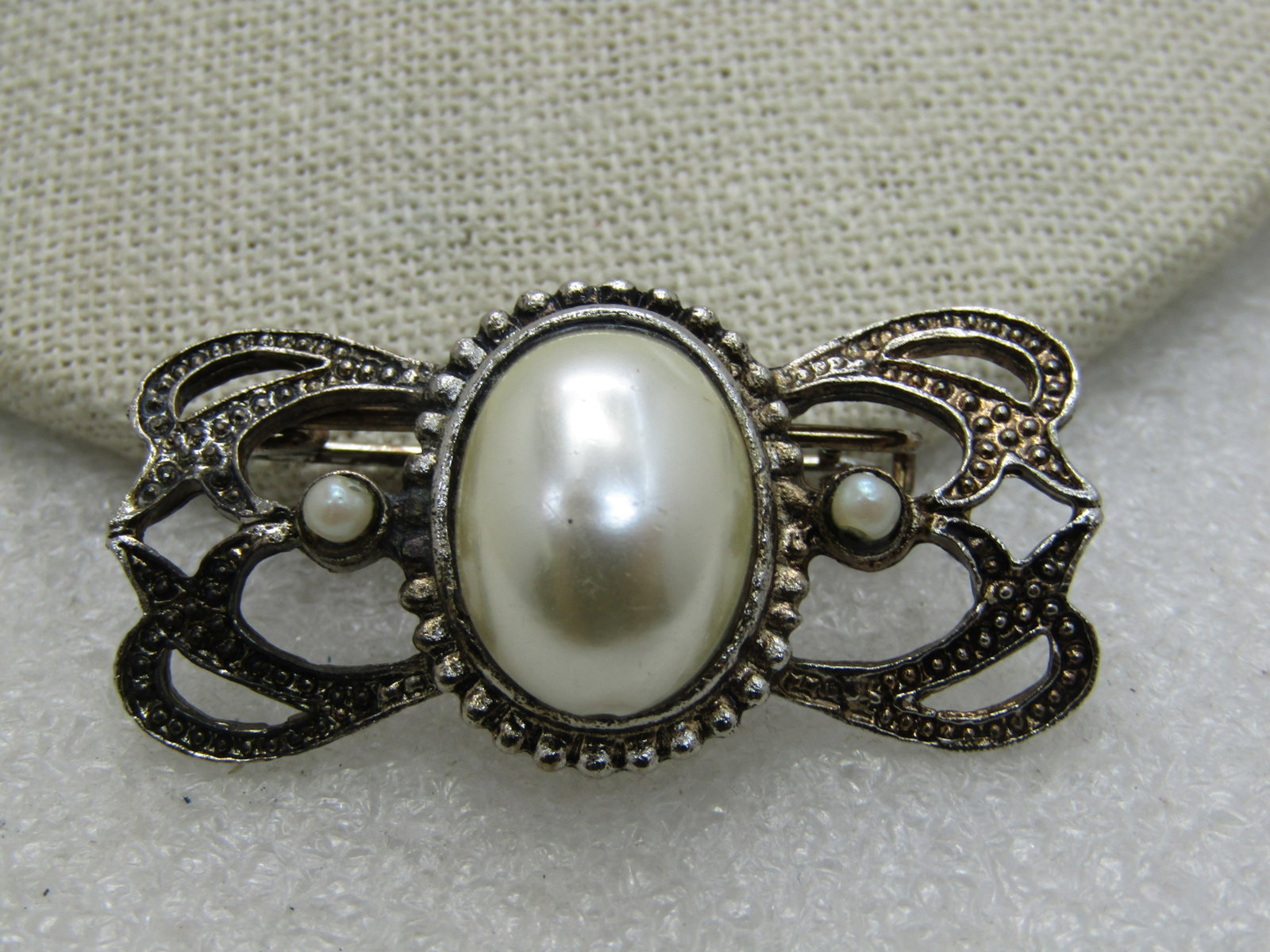 Vintage Faux Pearl Victorian Themed Brooch, 1.25": Vintage Faux Pearl Victorian Themed Brooch, 1.25" wide and 1" tall. A larged domed center faux pearl, bezel-set with a seed pearl on either side and a faux marcasite look. Not signed by the maker. Age