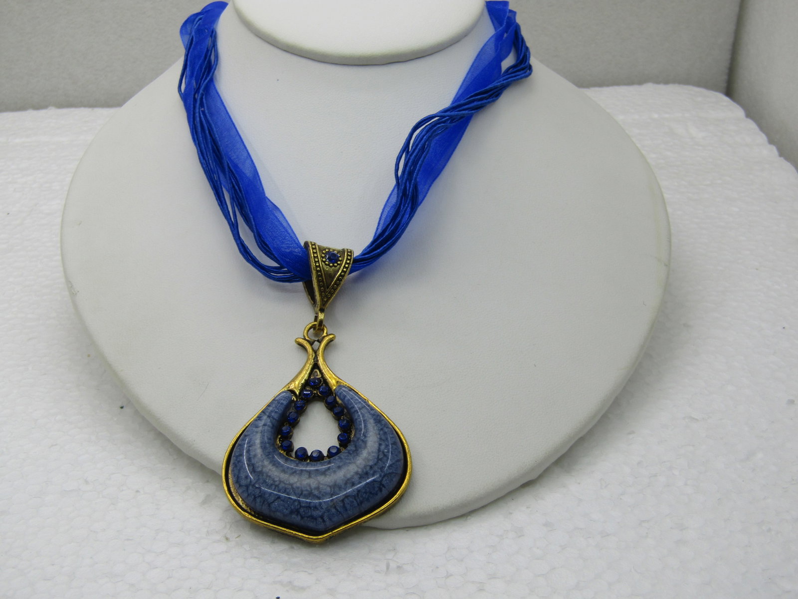 Blue Pendant on 16" Blue Multi-Strand Ribbon Necklace with Rhinestones: Blue Pendant on 16" Blue Multi-Strand Ribbon Necklace with RhinestonesTwo royal blue ribbon strands and 8 matching cord strands with a Gold tone slide with a d rop pendant with a total length of 3"