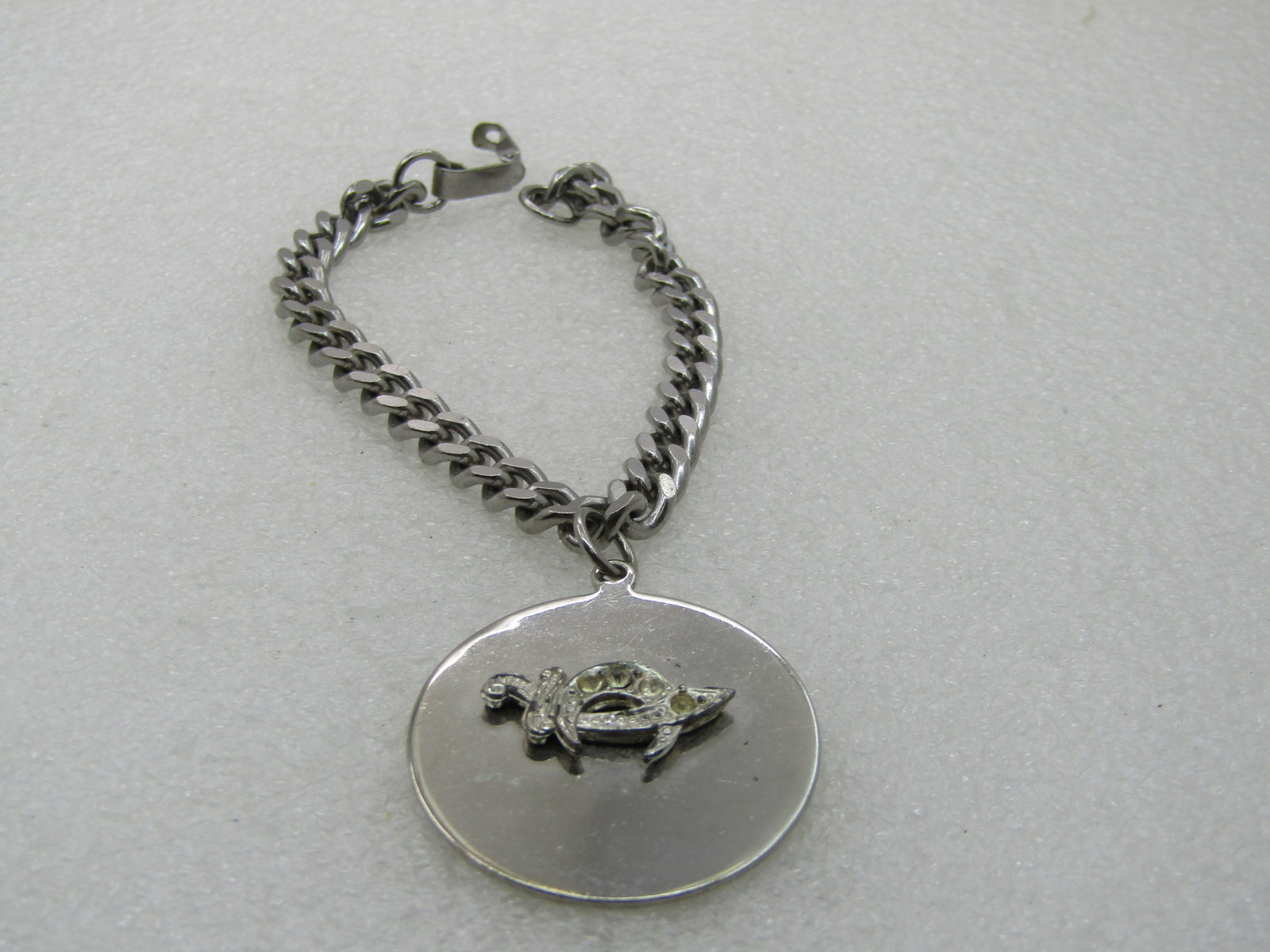 Vintage Shriner's Rhinestone Saber Charm Bracelet, 7", Stainless: Vintage Shriner's Rhinestone Saber Charm Bracelet, 7", Stainless Steel. 6mm wide chuky curb link chain with flip clasp. The charm is 1.25" round with a silver tone clear rhinestone saber mounted on