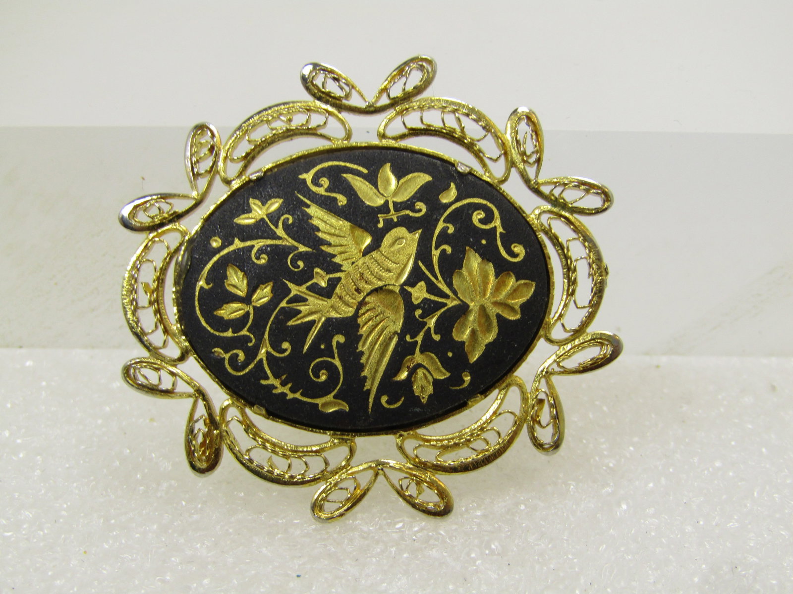 Vintage Damascene Bird Brooch, 1970's-1980's: Vintage Damascene Bird Brooch, 1970's-1980's. Gold filigree frame and gold tone with black background and engraved gold tone bird and leaves and scrolled design. Locking clasp. It is and ovalish shape