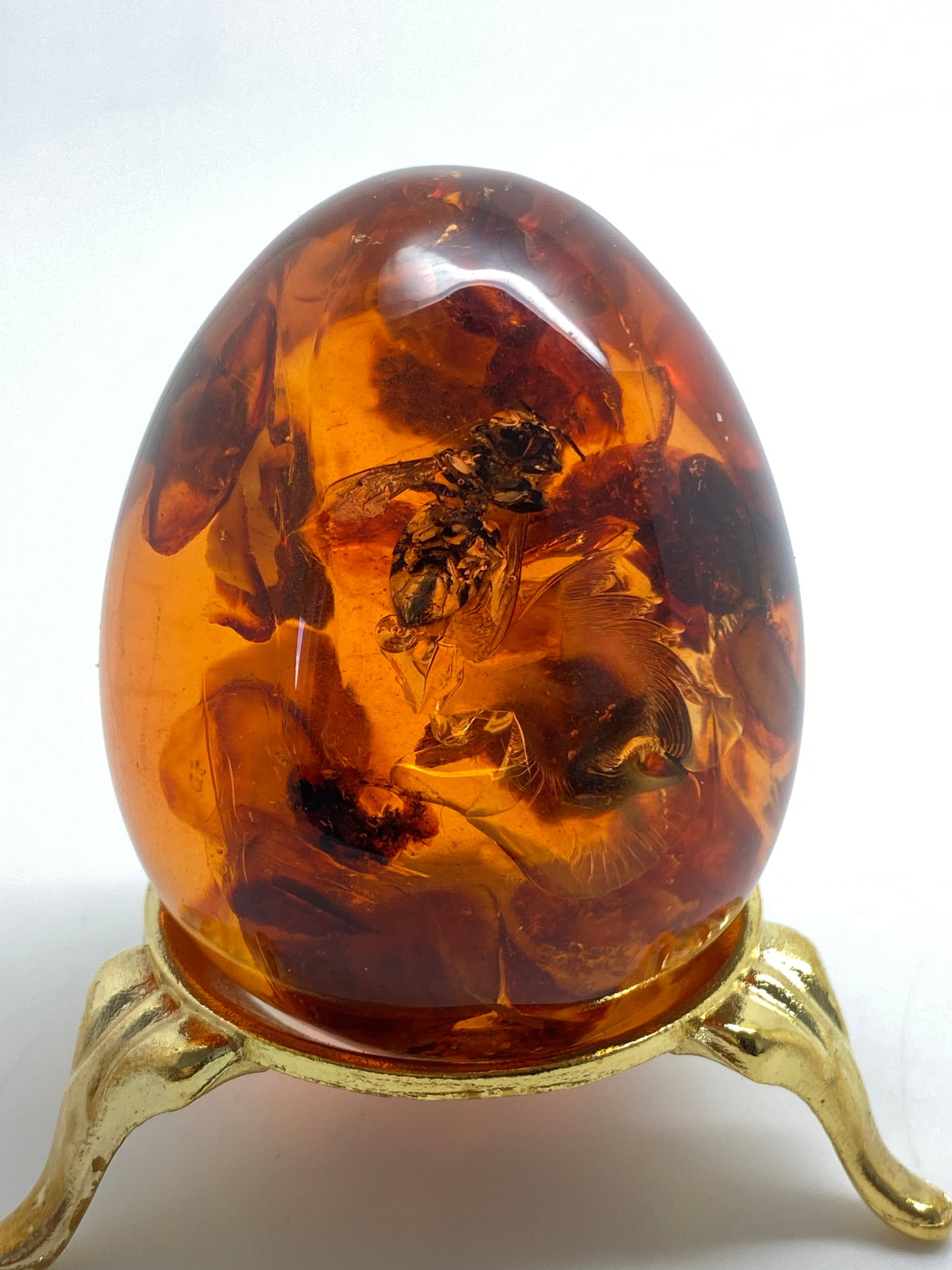 Stunning Amber Egg on a pedestal with insect inclusion: Title: Stunning Amber Egg on a pedestal with insect inclusion Metal: None Gemstone: Amber Weight: 72.7 g Size: Size: 56.7 x 45.0 x 45.0 mm Size: 2.232 x 1.772 x 1.772 inches Made of: (Reconstituted