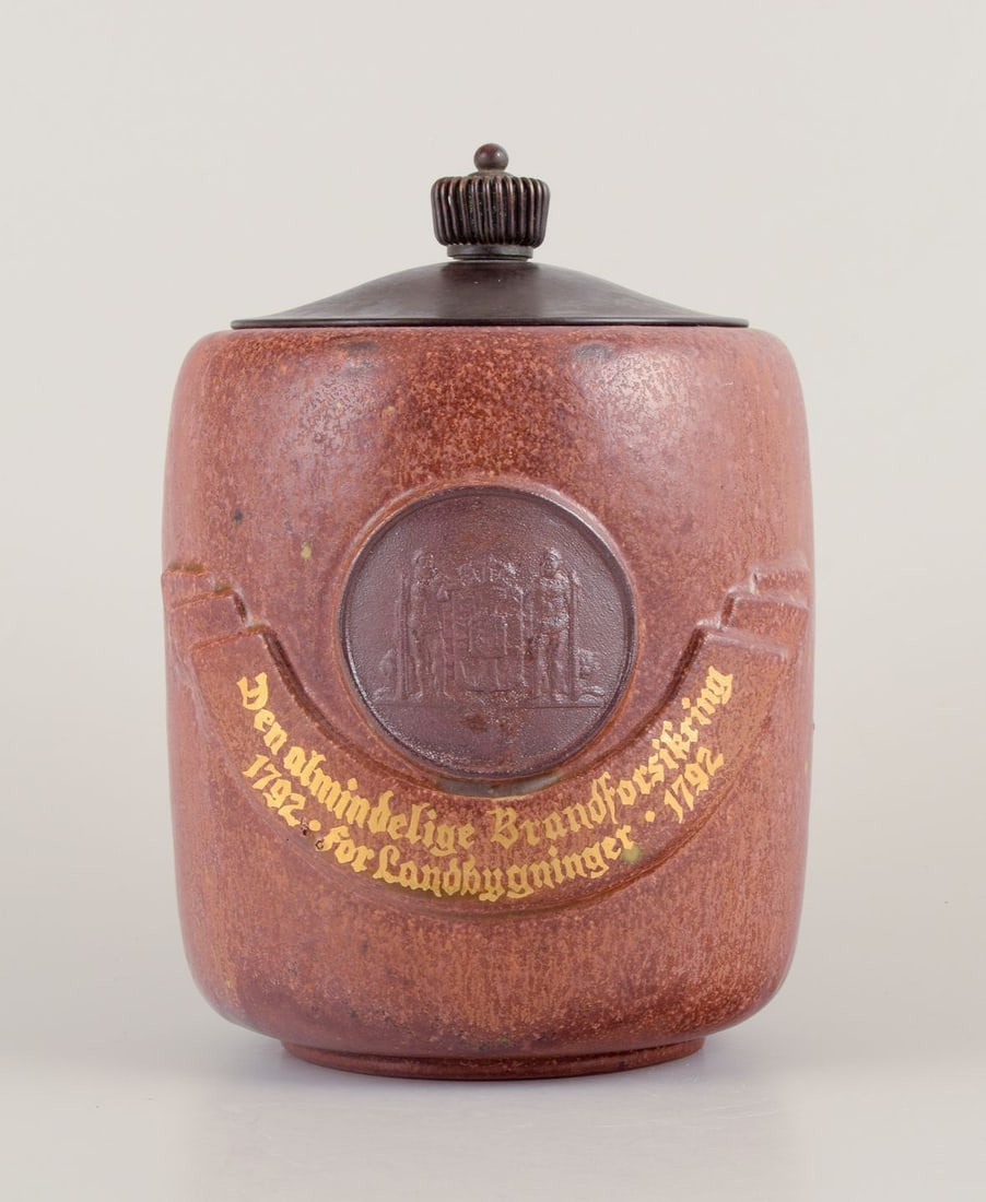 Arne Bang, Denmark. Lidded jar in glazed ceramic in shades of brown. Mid-20th C.: Arne Bang, Denmark. Own workshop. Lidded jar in glazed ceramic. Beautiful glaze in shades of brown. Lid of patinated metal. Text: "Den almindelige Brandforsikring 1792 for Landbygninger". Mid 1900s. I