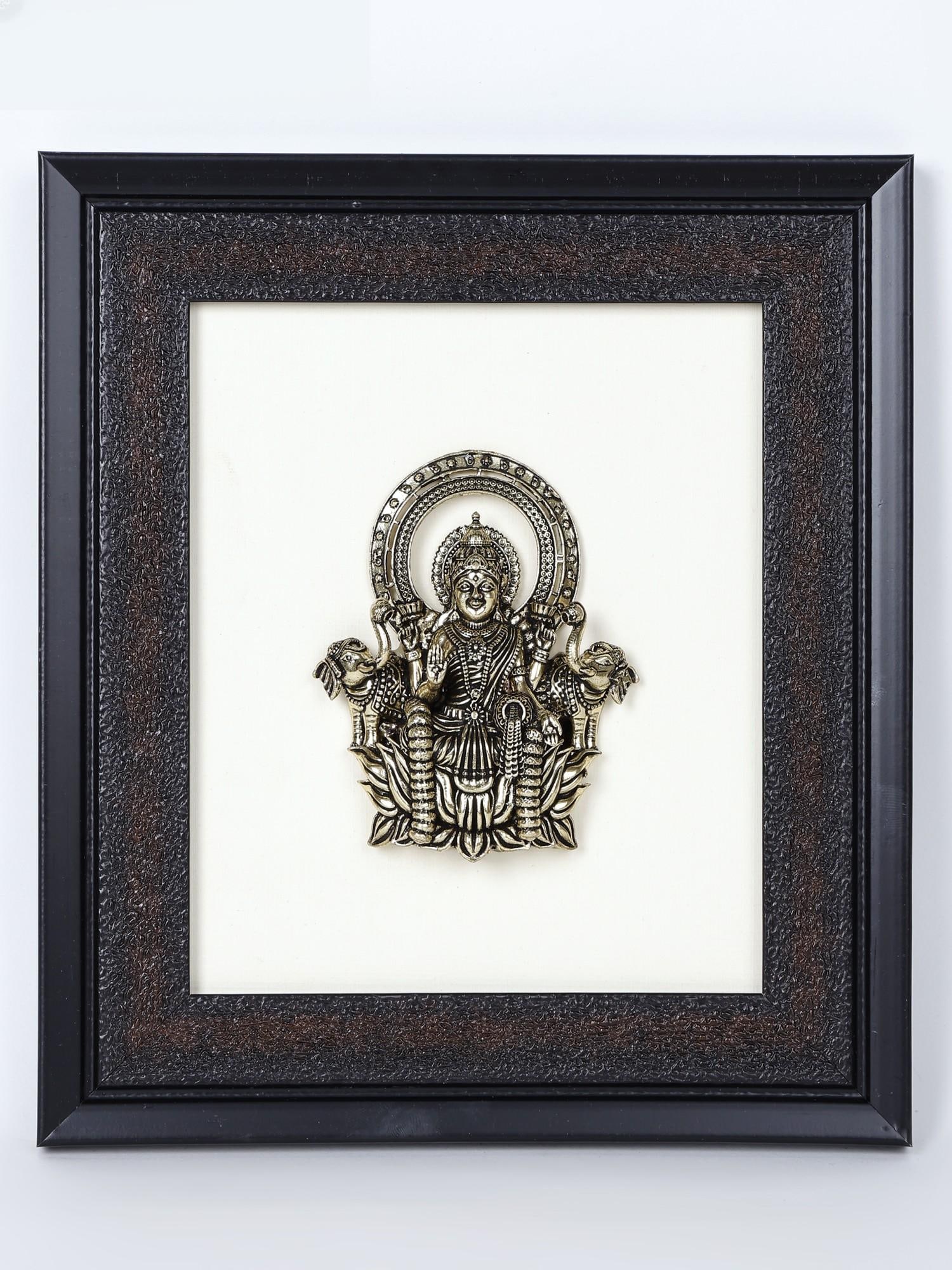 9" Superfine Goddess Gajalakshmi Wood Framed Brass Sculpture /Wall Hanging Statue: Description: The maternal and powerful aura of the ancient form of the Hindu goddess of wealth-Gajalakshmi , is luxuriously depicted in this brass and wood wall hanging. A plain white backdrop, symbol