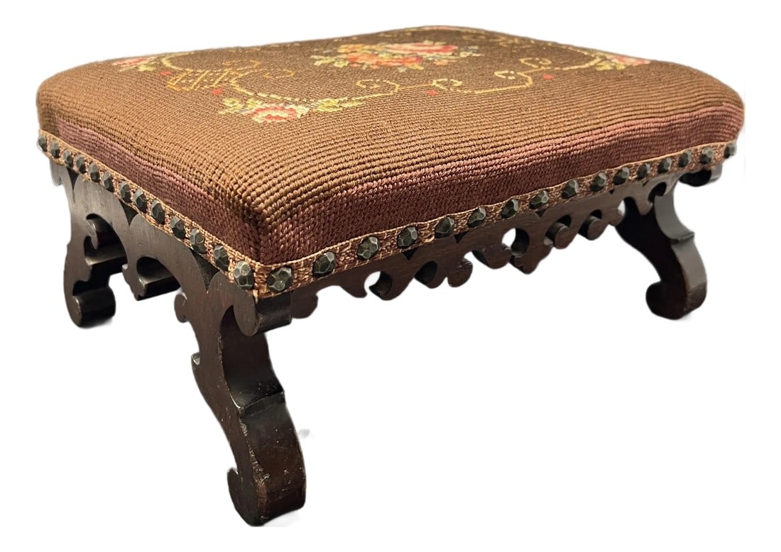 Antique Victorian Carved Walnut Needlepoint Footstool With Floral Embroidery: A charming antique Victorian footstool featuring a beautifully carved hardwood base and hand-worked floral needlepoint upholstery. The stool rests on graceful scrolling cabriole legs with a pierced