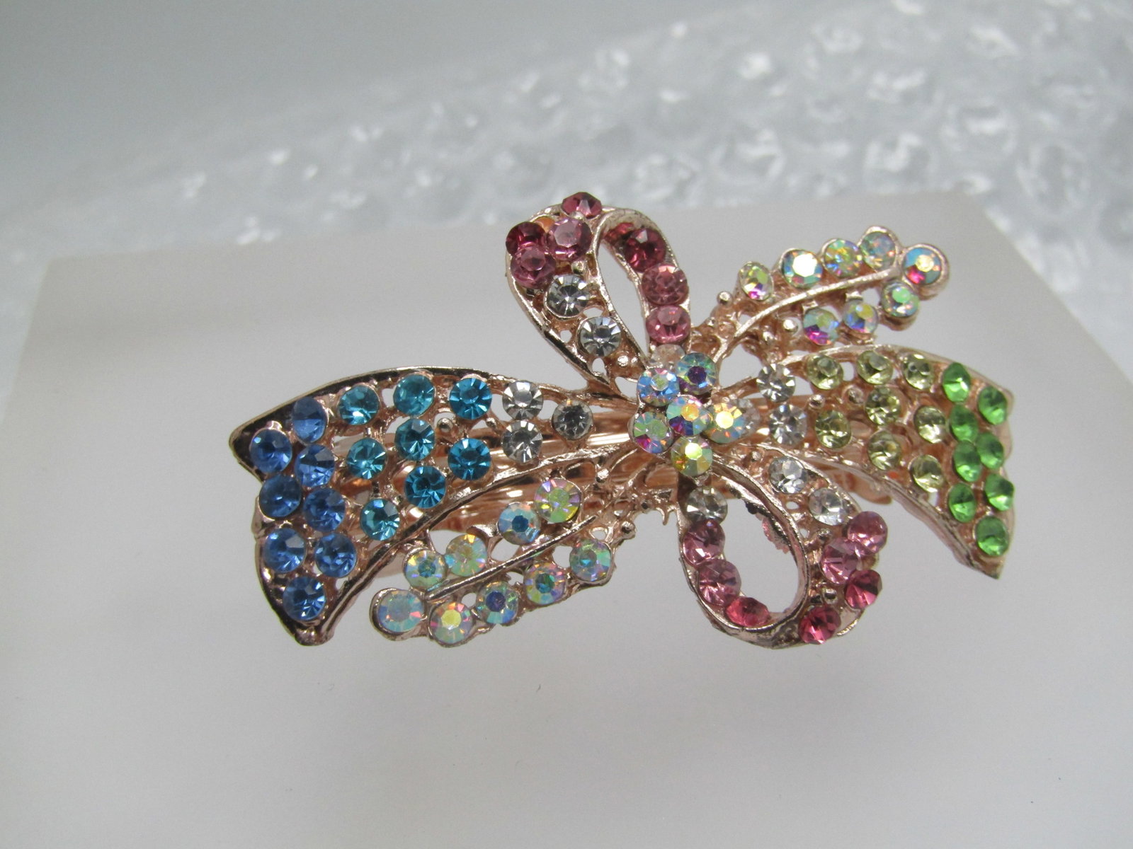Rose Gold Tone Rhinestone Bow Barrette. 2.25" by 1.5": Rose Gold Tone Rhinestone Bow Barrette. 2.25" by 1.5". Rhinestones are AB clear stones, pink, teal, blue, green with a bow and blossom design. The age is more current 2000 and after. it is not signed 