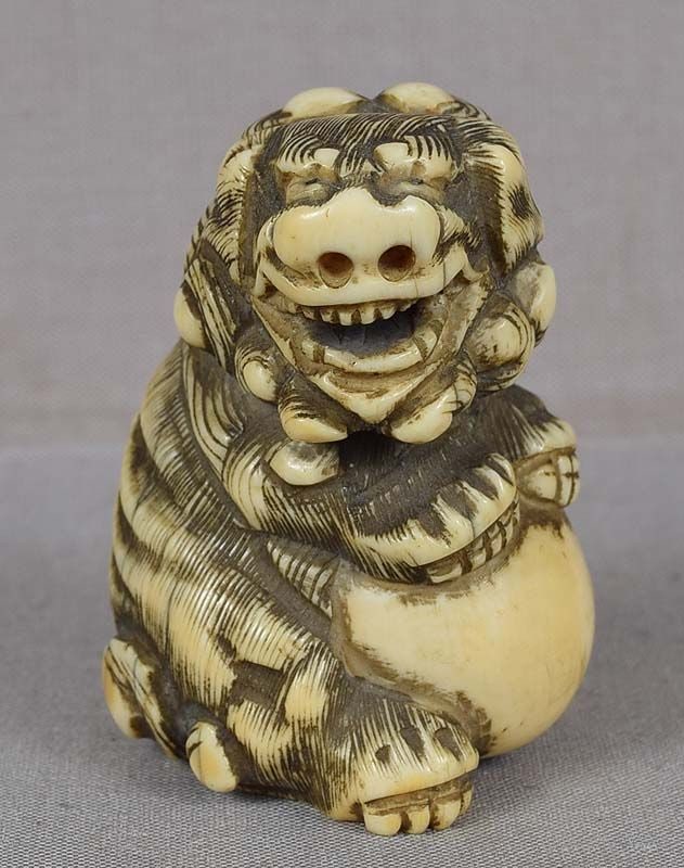 18c netsuke SHISHI with ball: Chunky 18th century netsuke of a sitting shishi (Buddhist lion) with its front paws on a ball. Great early carving with excellent depiction of its curly hair and powerful face, eyes are inlaid with bl