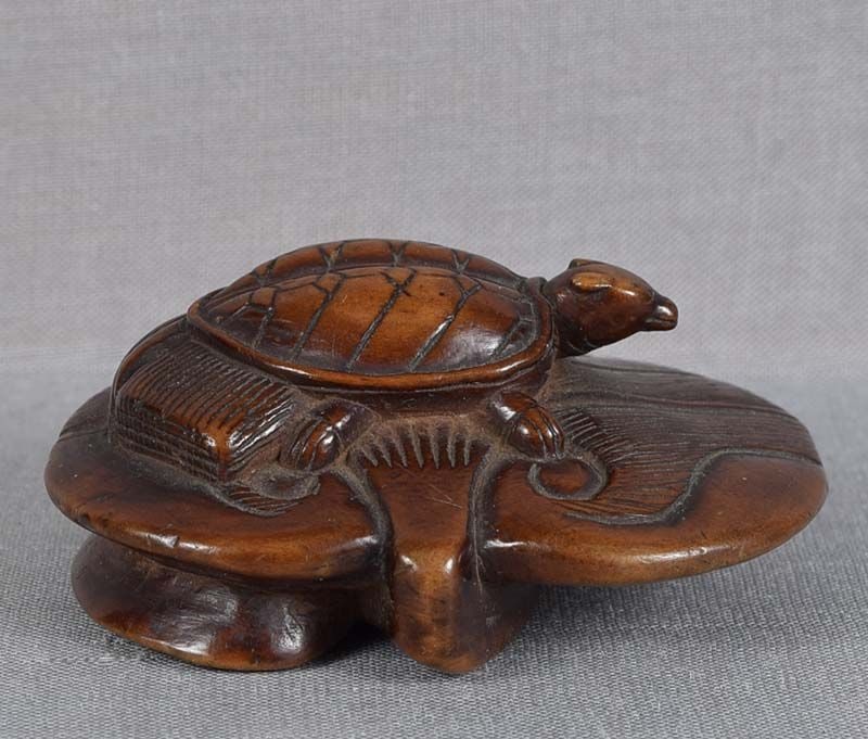 18c netsuke MINOGAME TURTLE on water lily: 18th century boxwood netsuke of minogame (turtle with dragon head and bushy tail, usually associated with longevity) sitting on water lily leaf. Strong early carving, great detailing of the turtle, it