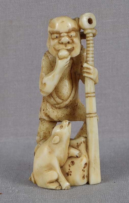 Early 19c marine netsuke ONI with club & PUPPY: Early 19th century marine (walrus tusk) netsuke of a standing oni, its foot on rockery, leaning on a huge war club and eating a rice cake, and a puppy at his feet looking wiistfully at the same cake.