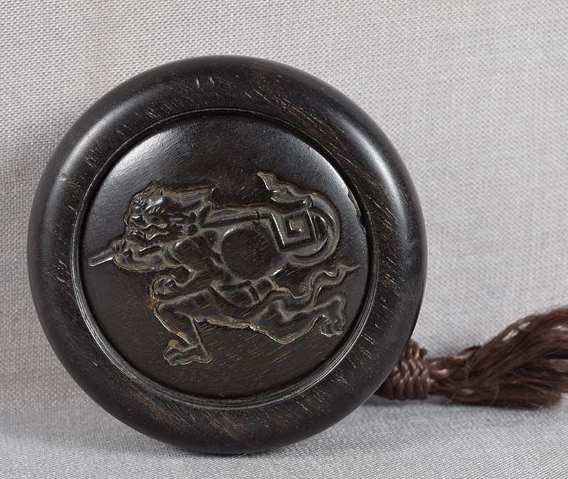 19c kagamibuta netsuke buffalo horn THUNDER GOD RAIDEN: 19th century netsuke of kagamituta (“mirror lid”) type with wooden bowl and buffalo horn top carved in sunken relief with a scene of running Thunder God Raiden beating his drum, thus