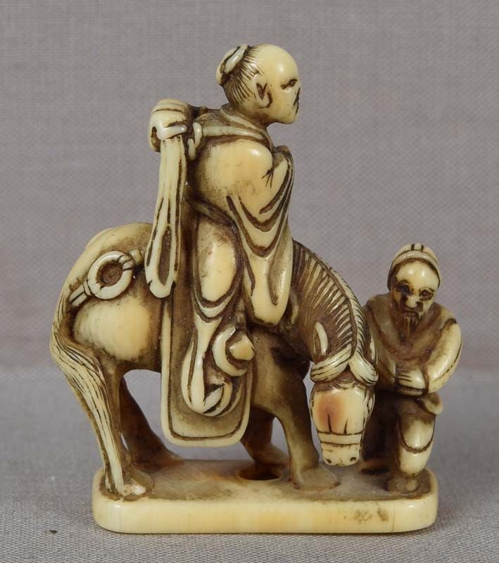 Early 19c netsuke TOBA on mule with attendant: Early 19th century netsuke of Chinese official, poet and calligrapher Toba with a bundle of books on his back riding on a mule accompanied by an attendant. Toba was removed from his post and sent