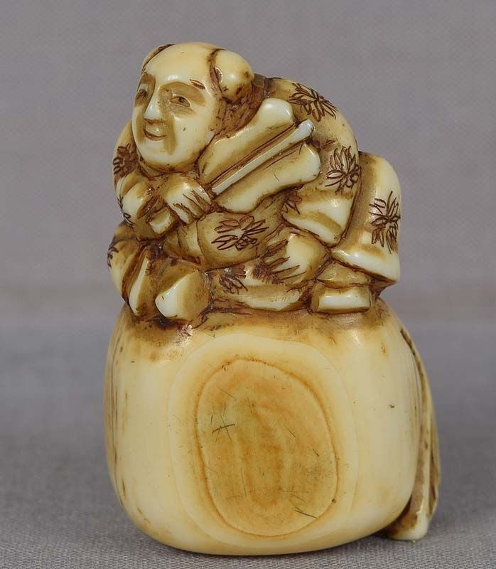 18c netsuke BOY on bag: 18th century netsuke of a karako (Chinese boy) wearing nicely decorated robe, holding a fan in his hand and seating on a very large bag. Strong early netsuke, great facial expression with an